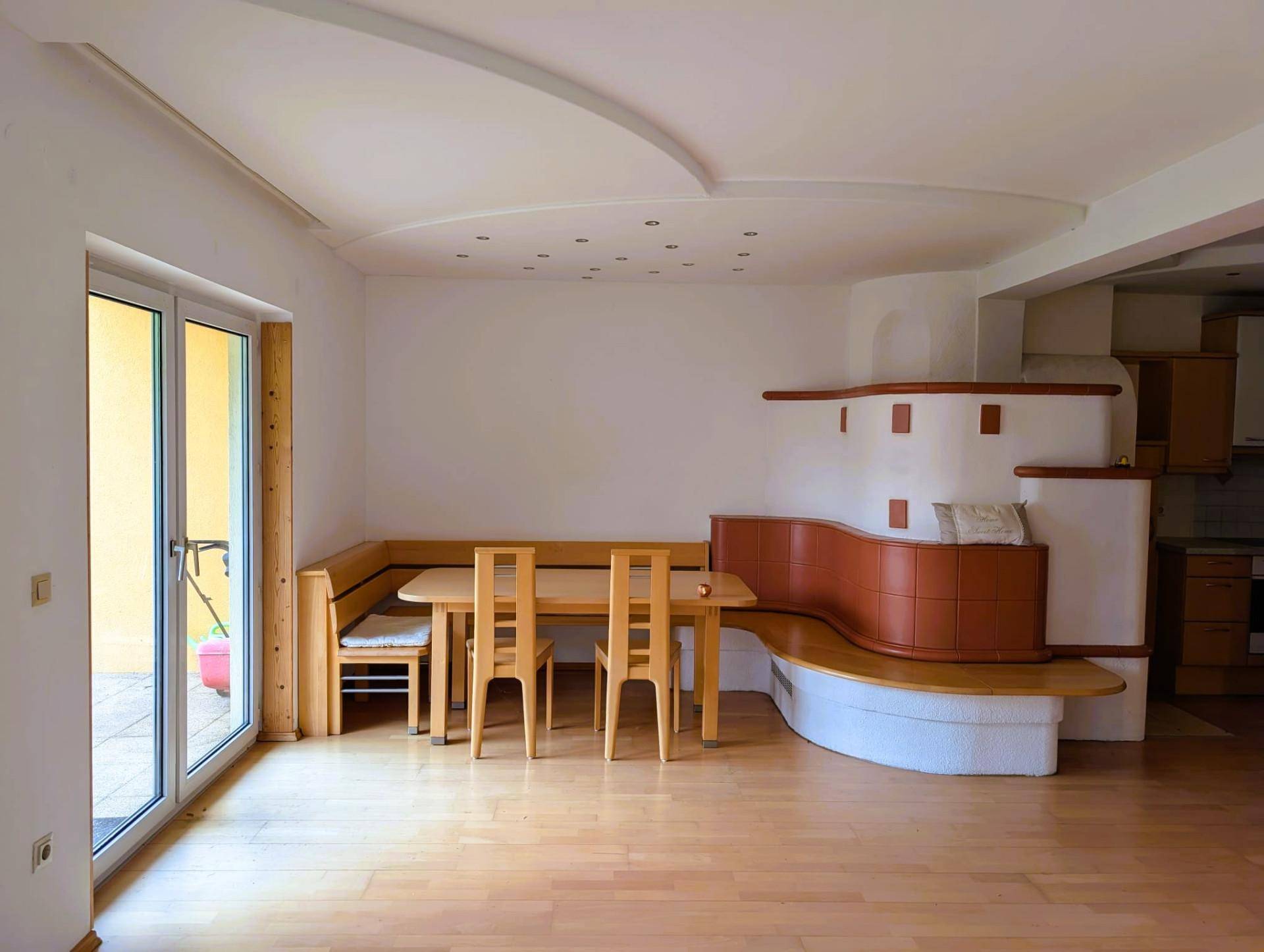 Geräumiger Wohn-Essbereich mit Kachelofen, Holzboden und Zugang zur Terrasse.
