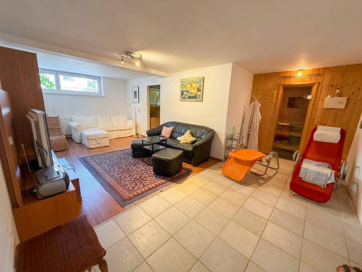 Ausgebauter Kellerbereich mit Wohnzimmer, Fliesenboden und Zugang zur Sauna.