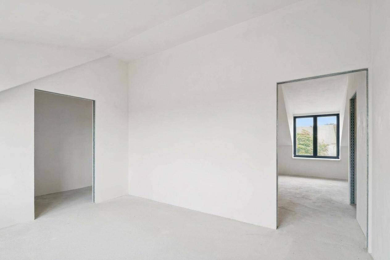 Dachgeschossraum im Rohbau mit schrägen Wänden und einem Fenster, bereit für den Ausbau.