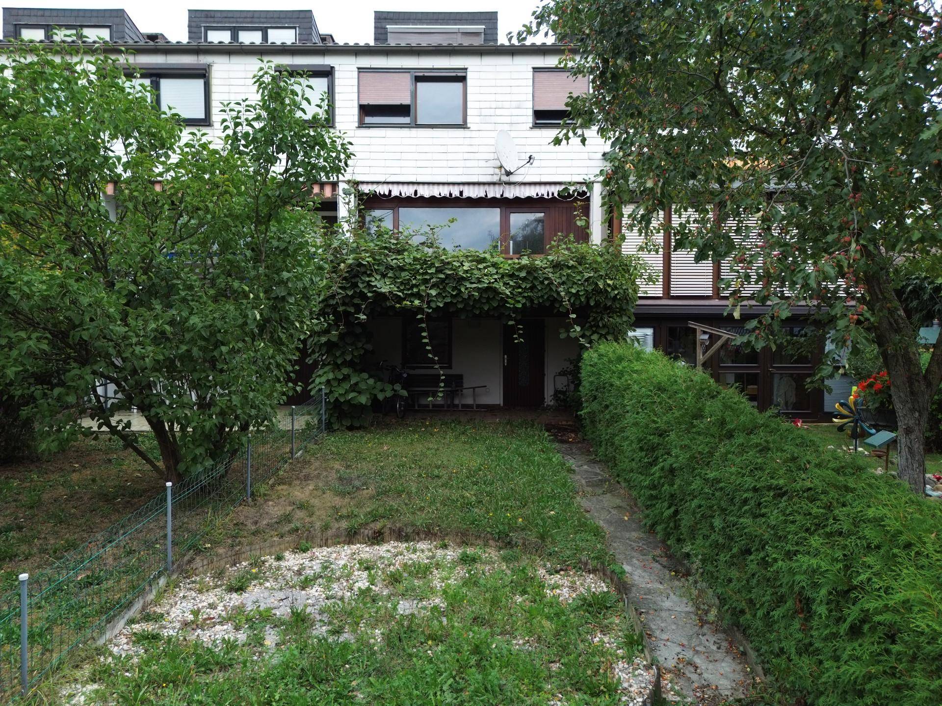 Hinterhofgarten der Reihenhäuser mit Rasenfläche, Hecke und Zugang zu einer überdachten Terrasse.