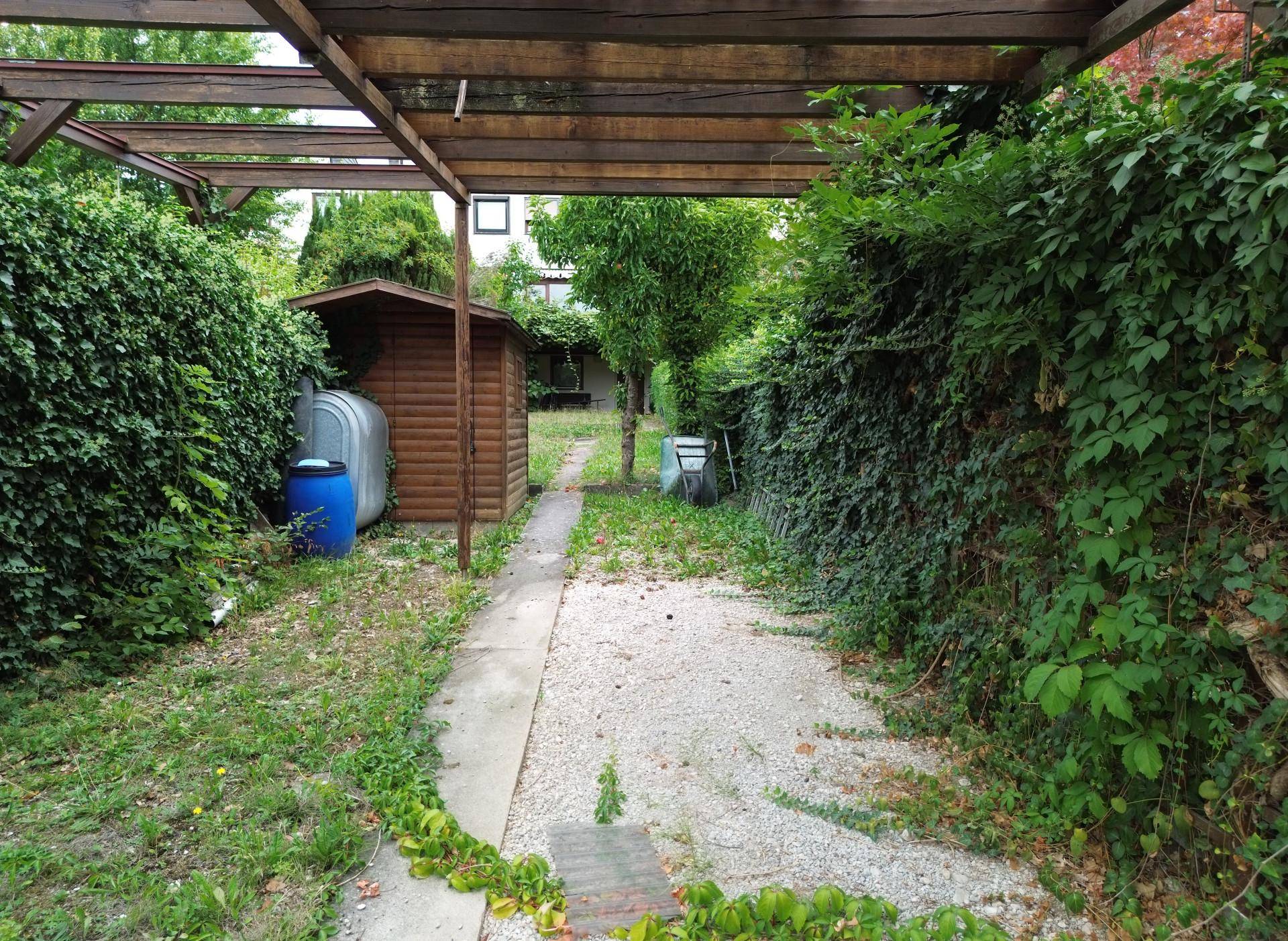 Gartenweg führt zu einem kleinen Gartenhaus, umgeben von üppigem Grün und einer Pergola.