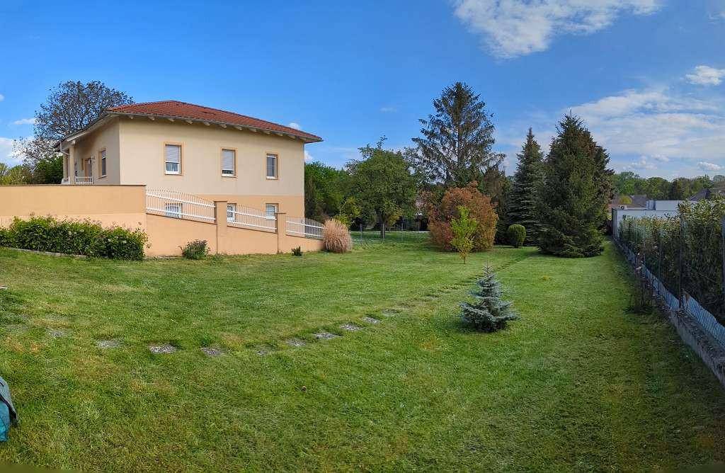 Weitläufiger Garten mit großer Rasenfläche vor einem hellen Wohnhaus unter strahlend blauem Himmel.