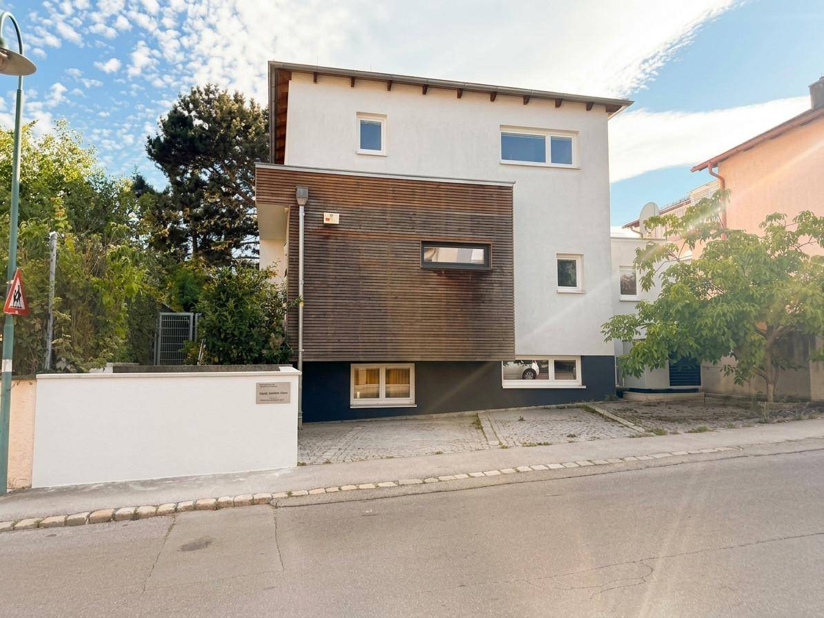 Moderne Hausfassade mit Holzverkleidung und großen Fenstern von der Straßenseite.
