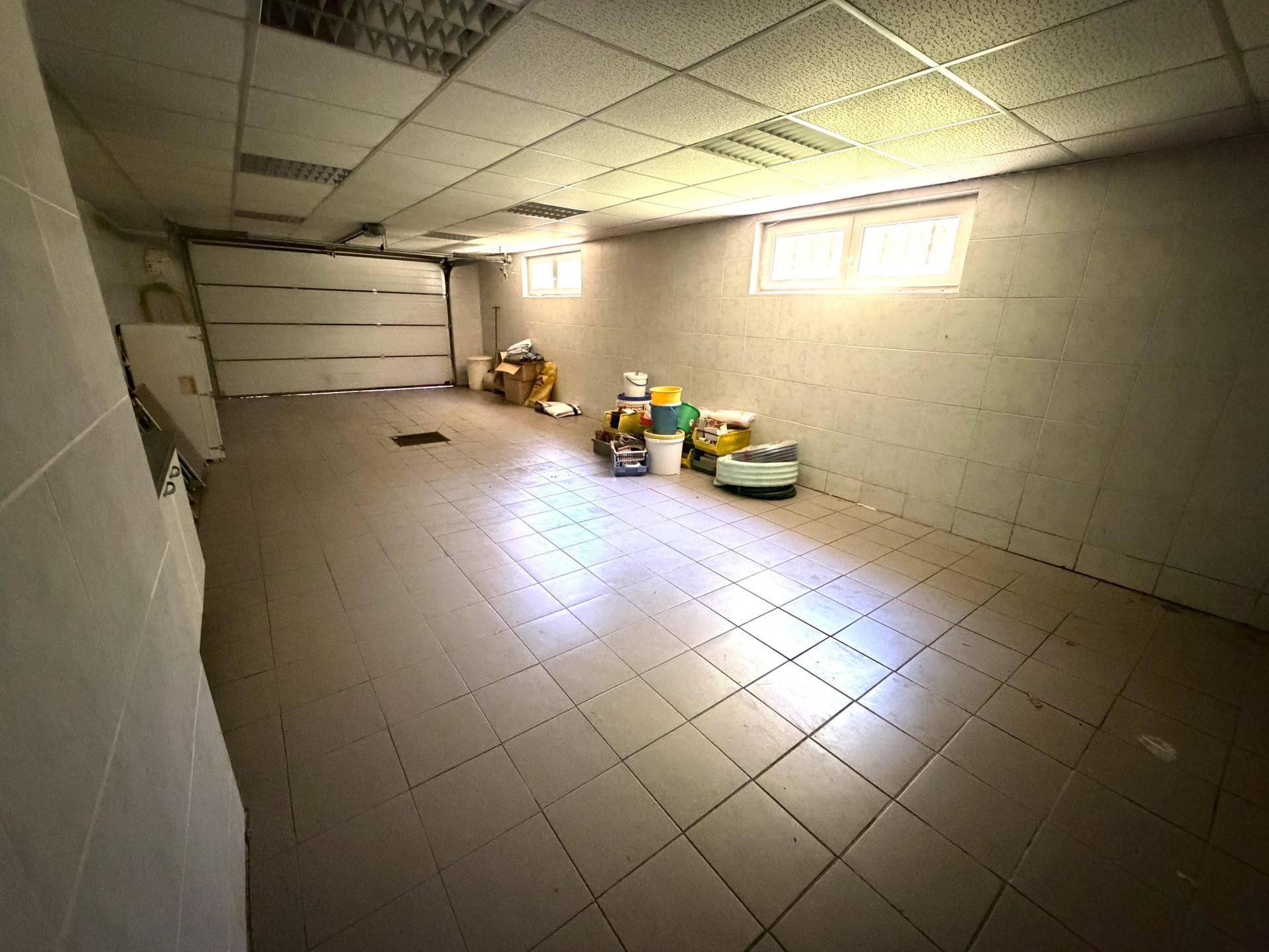 Geräumige Garage mit Fliesenboden, Rolltor und Fenstern für natürliche Belüftung.