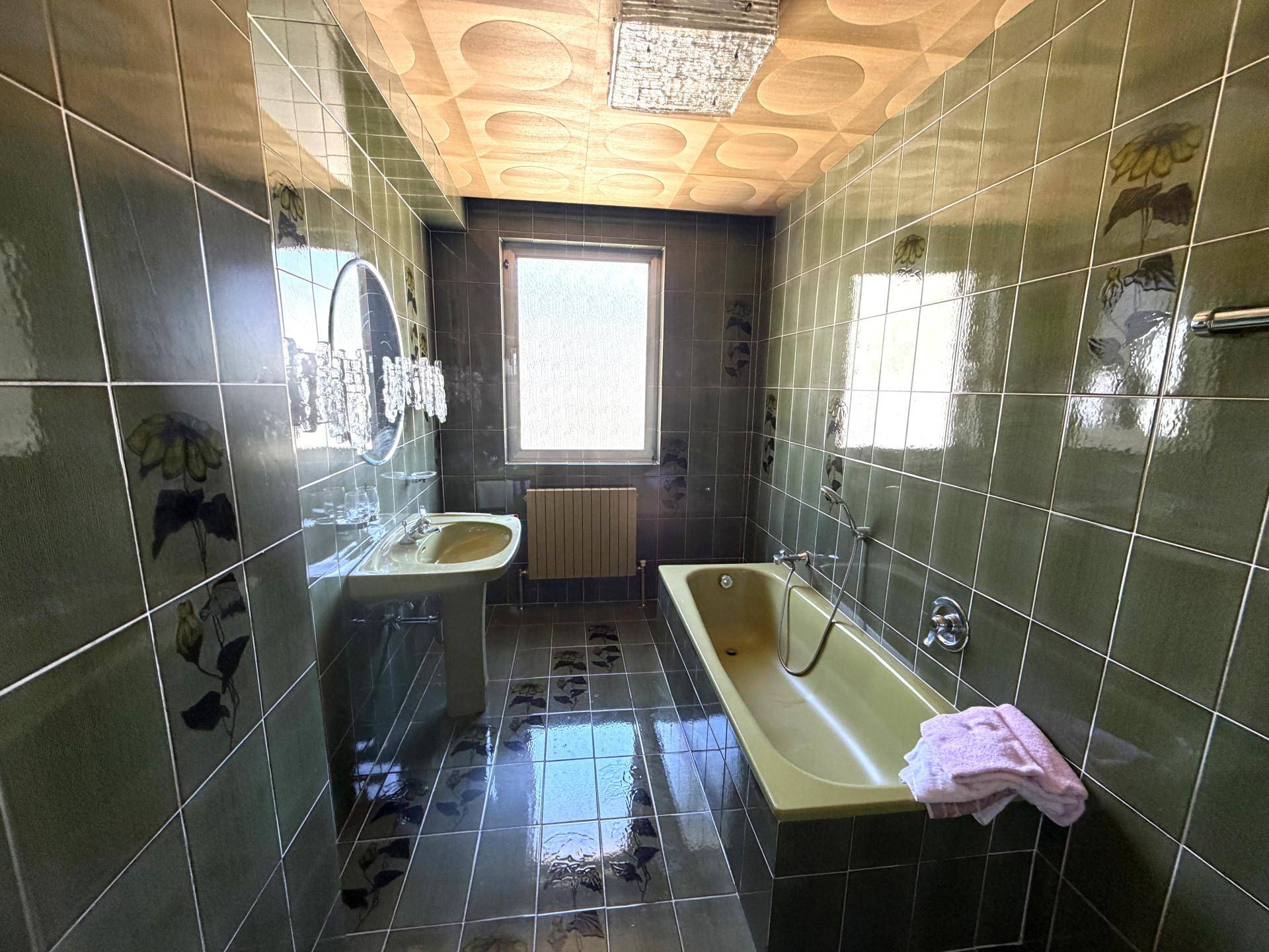 Badezimmer im 80er-Jahre-Stil mit grünen Fliesen, Badewanne und Fenster für Tageslicht.