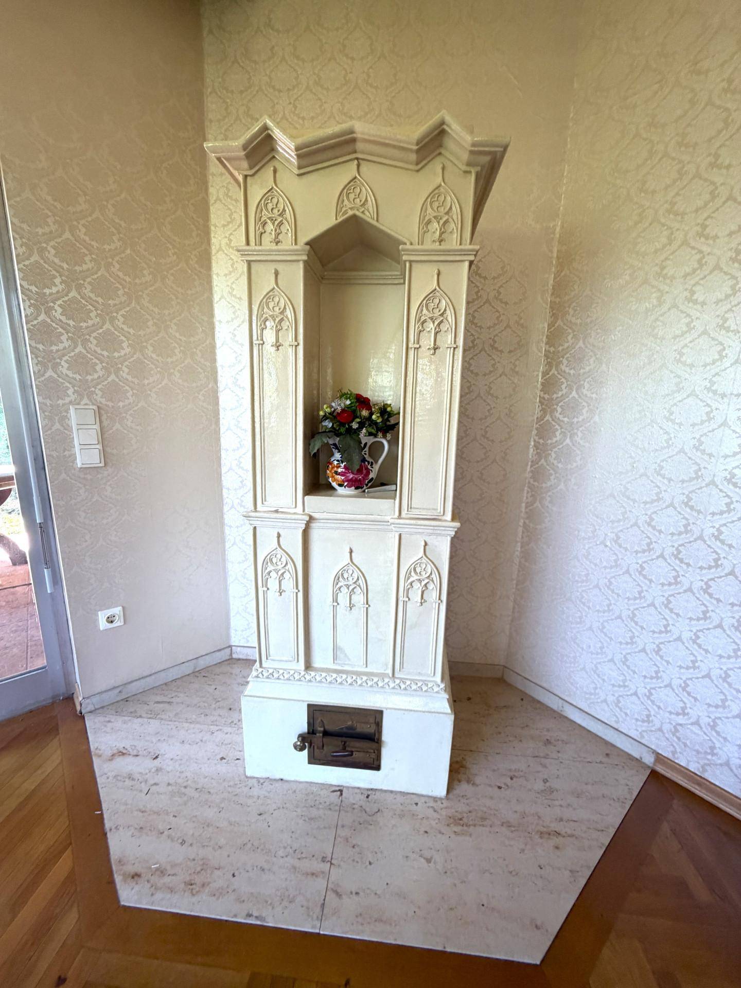 Detailansicht eines eleganten, weißen Kachelofens mit floralen Verzierungen im Wohnbereich.