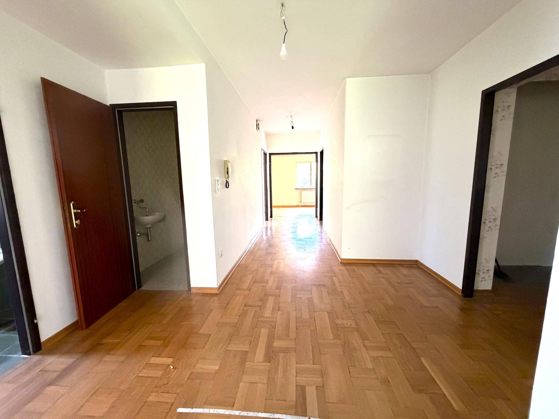 Langer Flur mit Parkettboden, weißen Wänden und Türen zu verschiedenen Räumen.