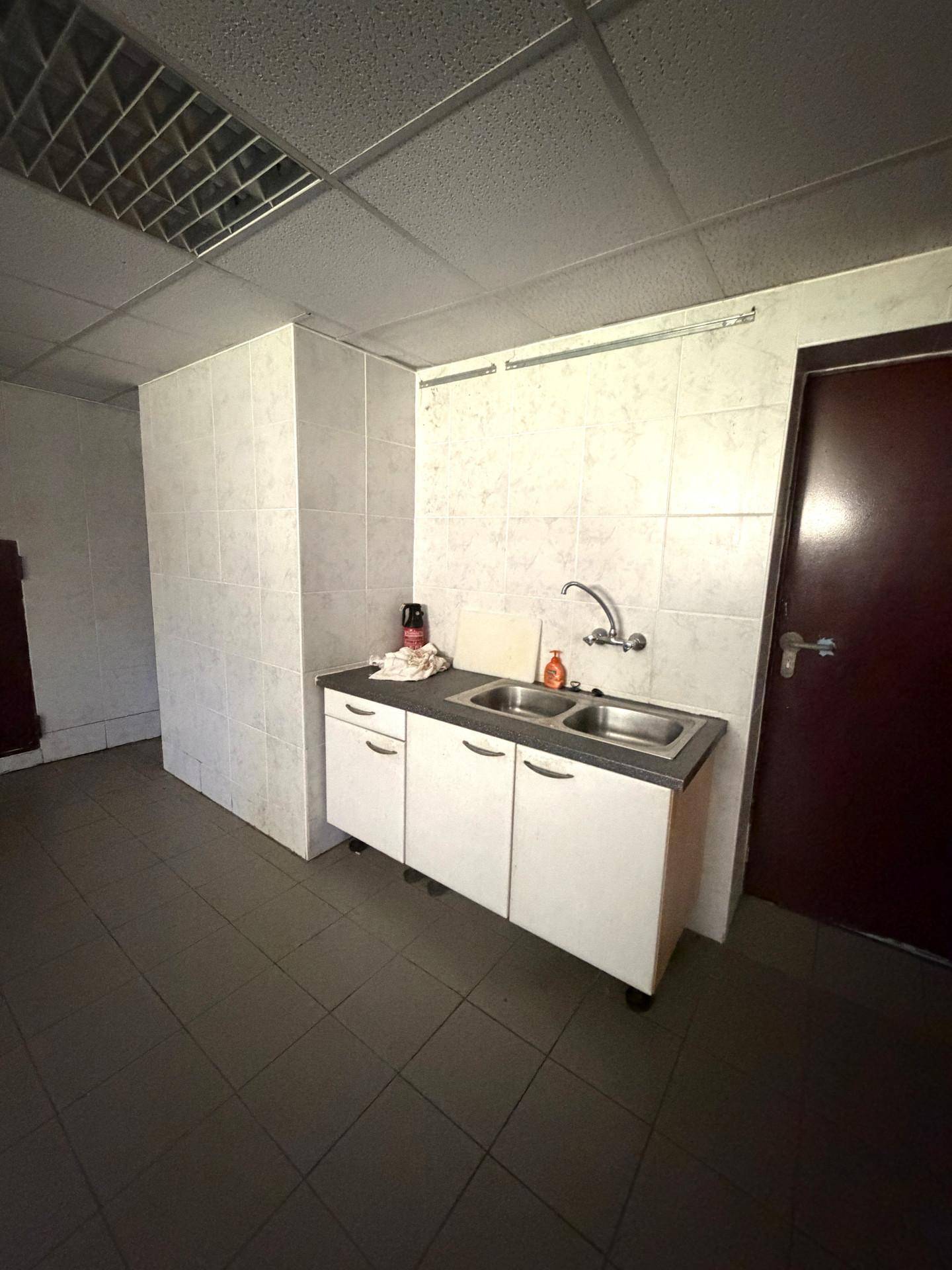 Einfacher Hauswirtschaftsraum mit Spülbecken und gefliesten Wänden, ideal für zusätzliche Lagerung.