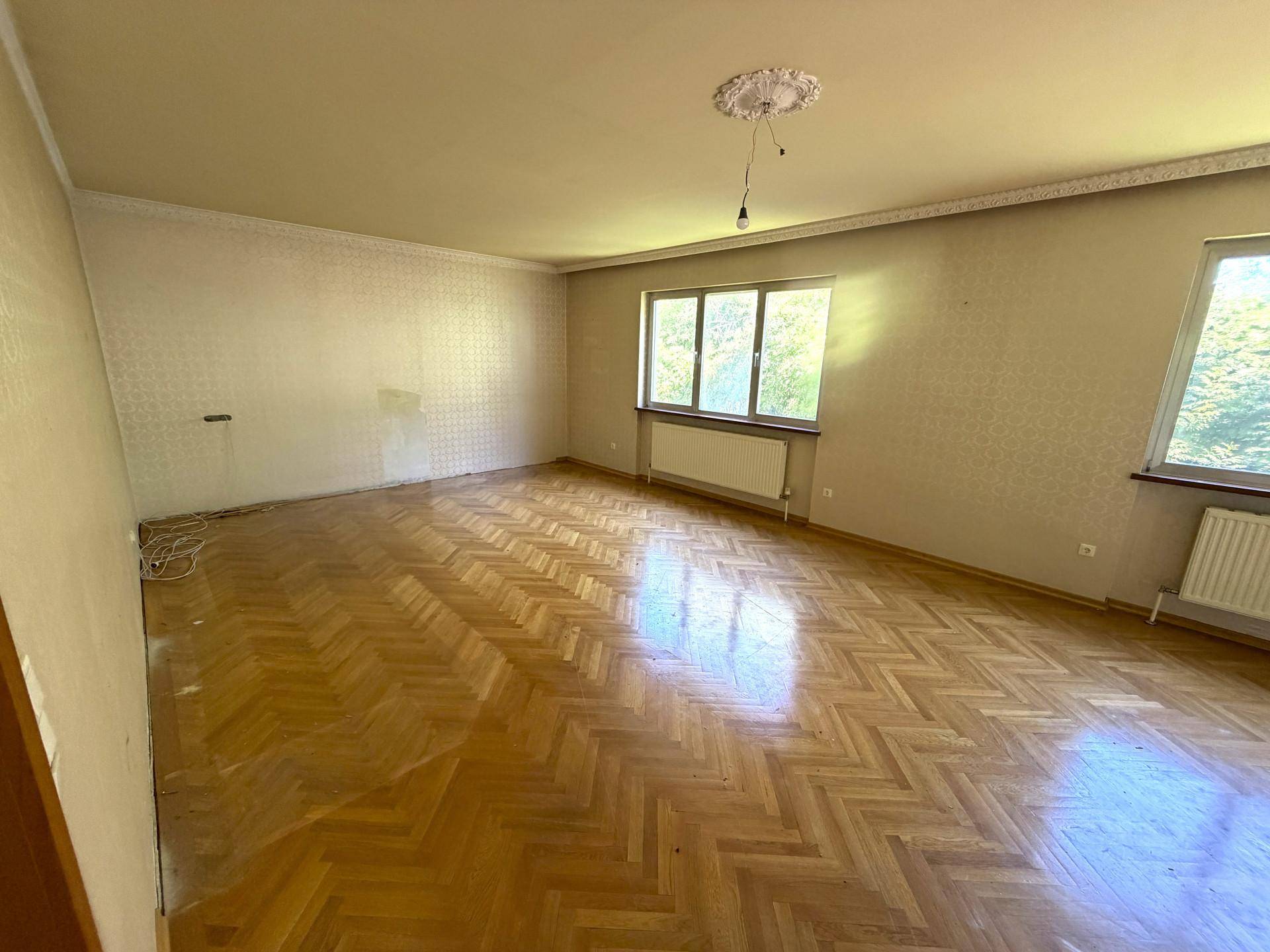 Geräumiges Wohnzimmer mit Fischgrätparkett, großen Fenstern und Zugang zur Terrasse.