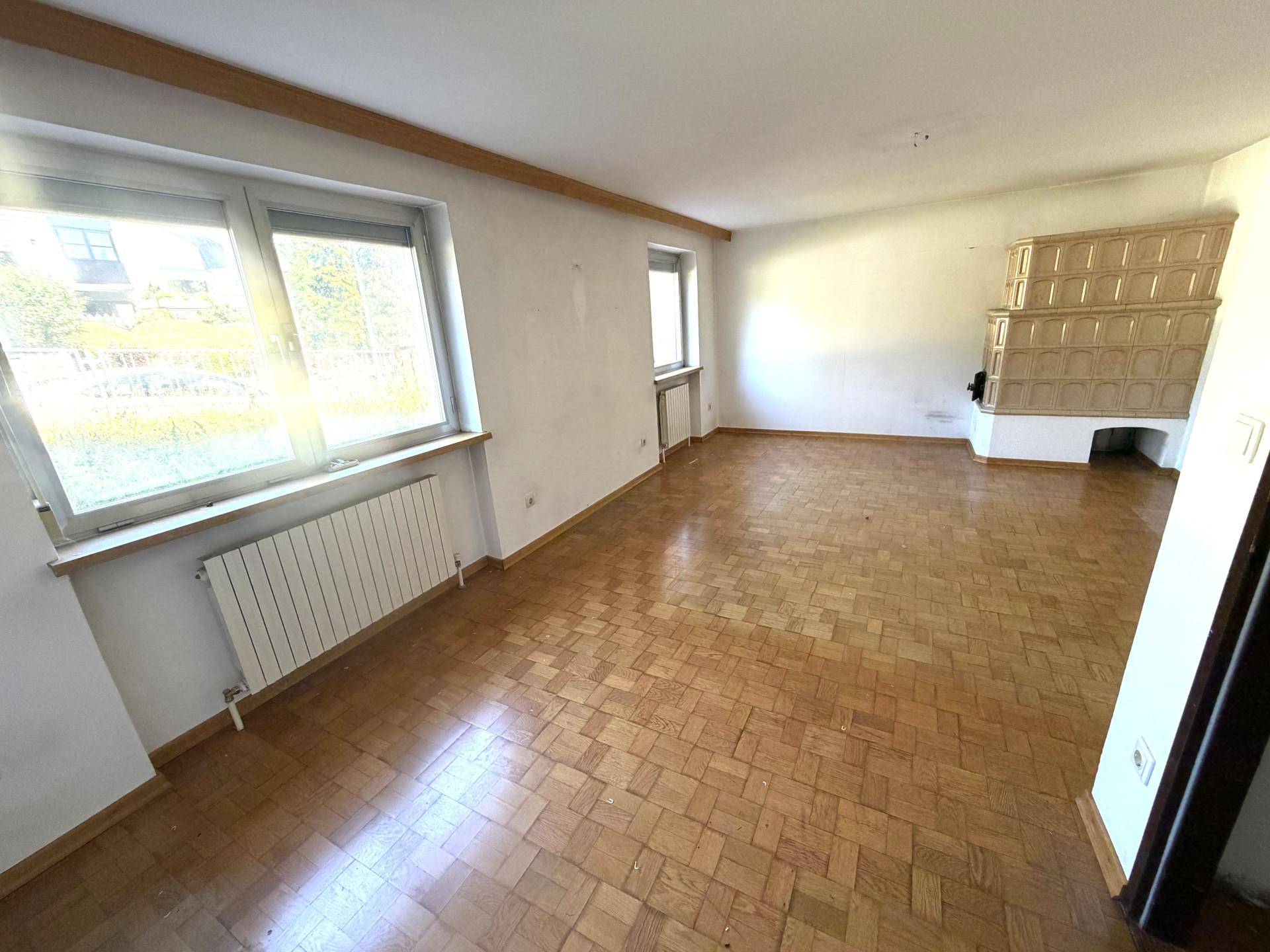 Helles Wohnzimmer mit Parkettboden und einem traditionellen Kachelofen als Blickfang.