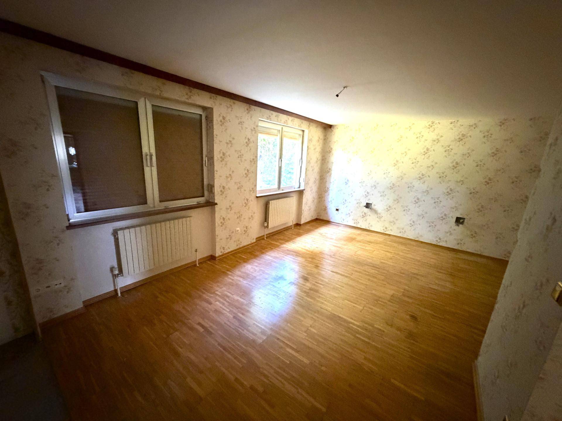 Schlafzimmer mit Parkettboden, floraler Tapete und zwei Fenstern für ausreichend Tageslicht.