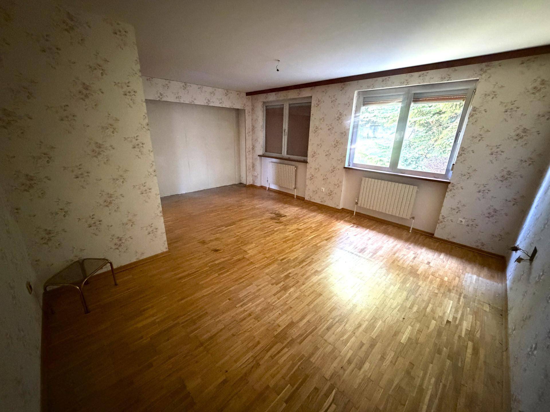 Schlafzimmer mit Parkettboden, floraler Tapete und zwei Fenstern für ausreichend Tageslicht.