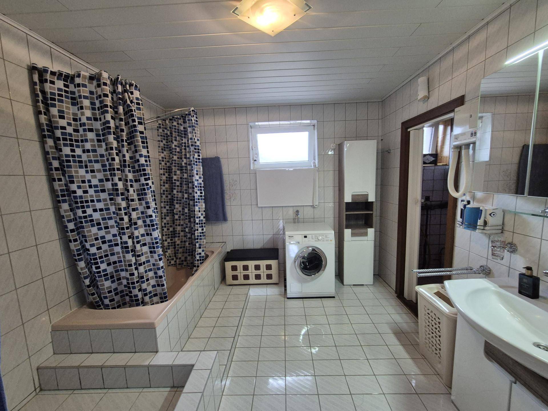 Gefliestes Badezimmer mit Badewanne, Dusche, Waschmaschine und Fenster.