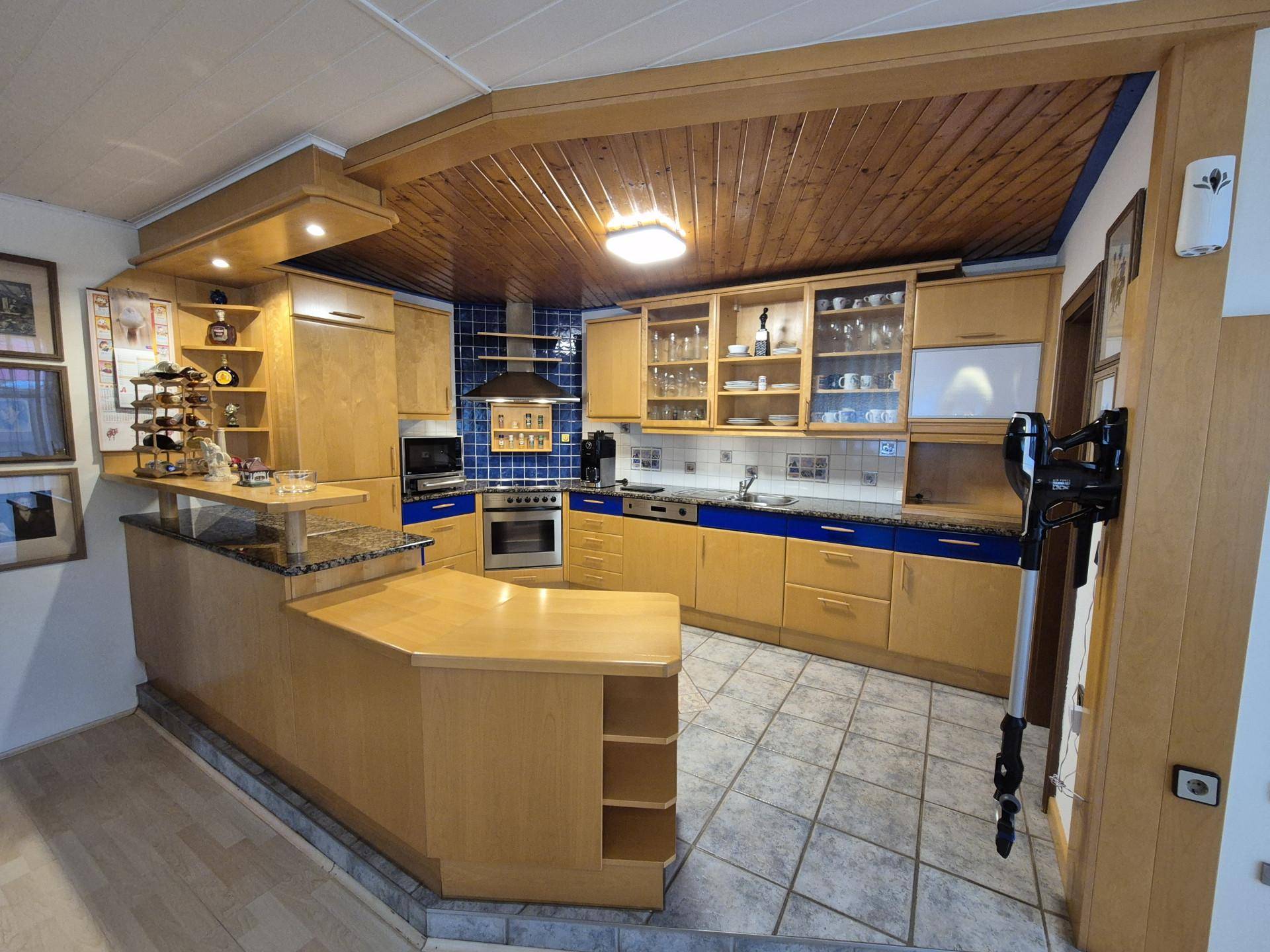 Geräumige Küche mit Holzschränken, blauen Akzenten und gefliestem Boden.