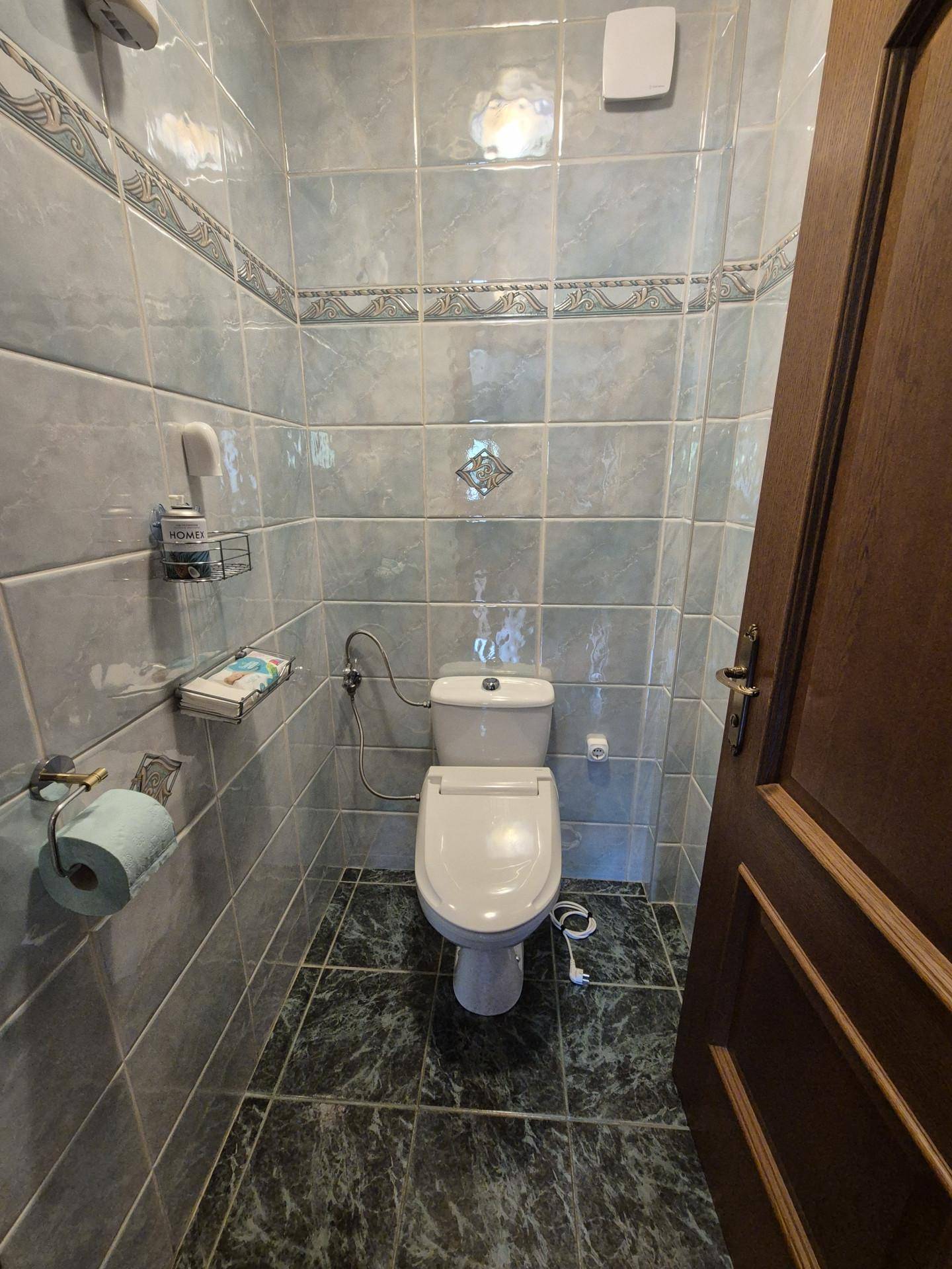 Kleines, gefliestes WC mit Toilette und Wandregal.