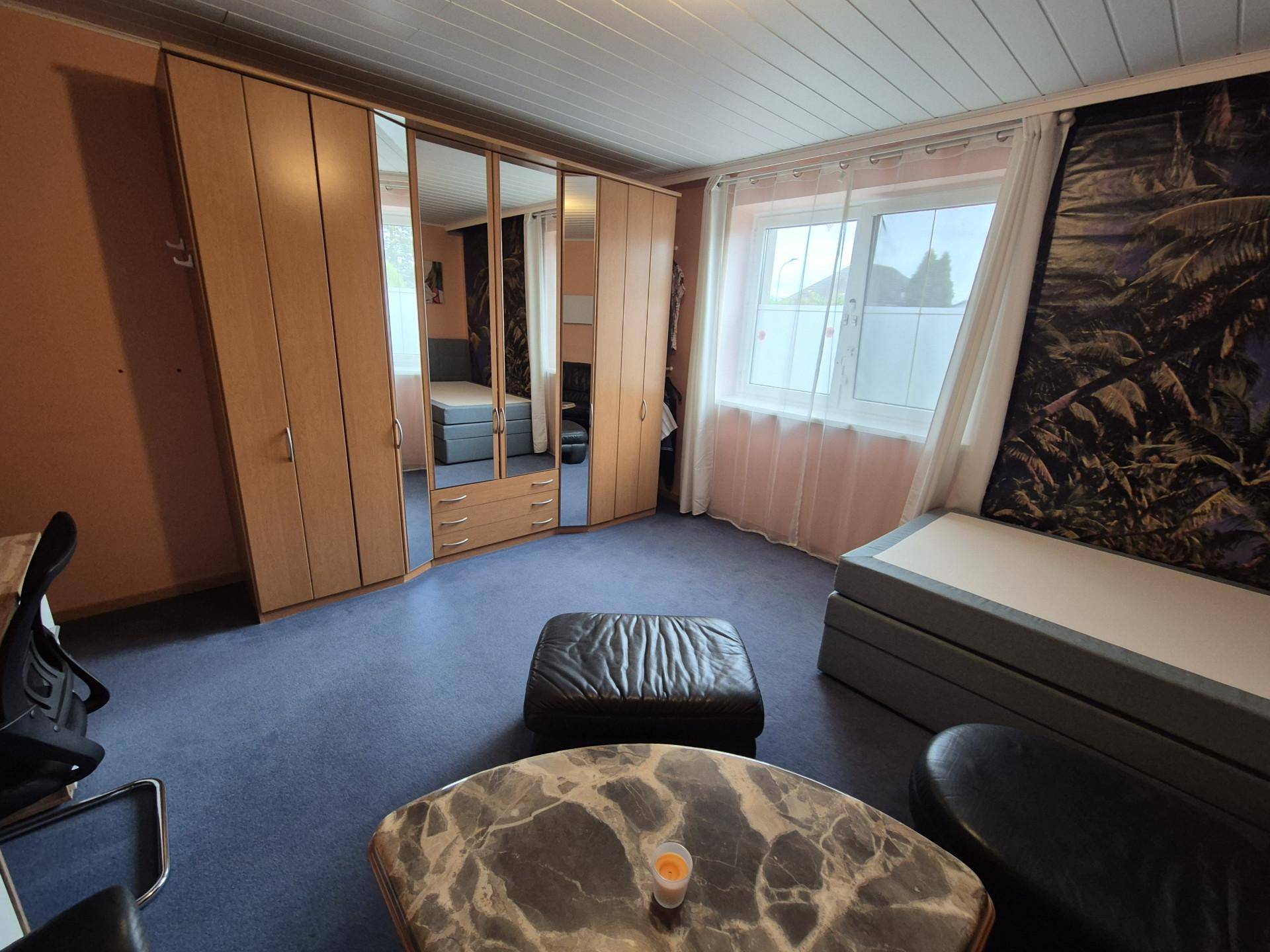 Schlafzimmer mit Teppichboden, Spiegelschrank und Fenster mit Blick nach draußen.