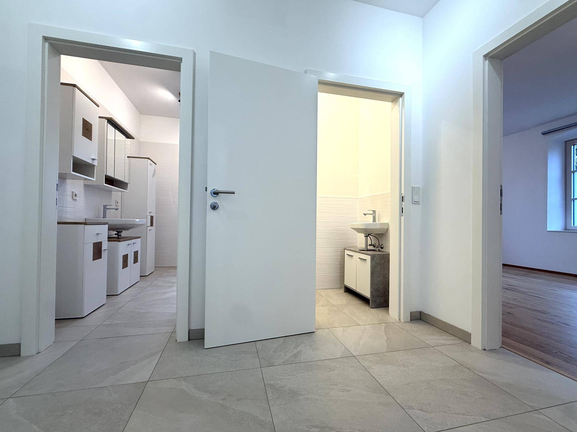Heller Flur mit Fliesenboden, der zu einem Badezimmer und einer separaten Toilette führt.