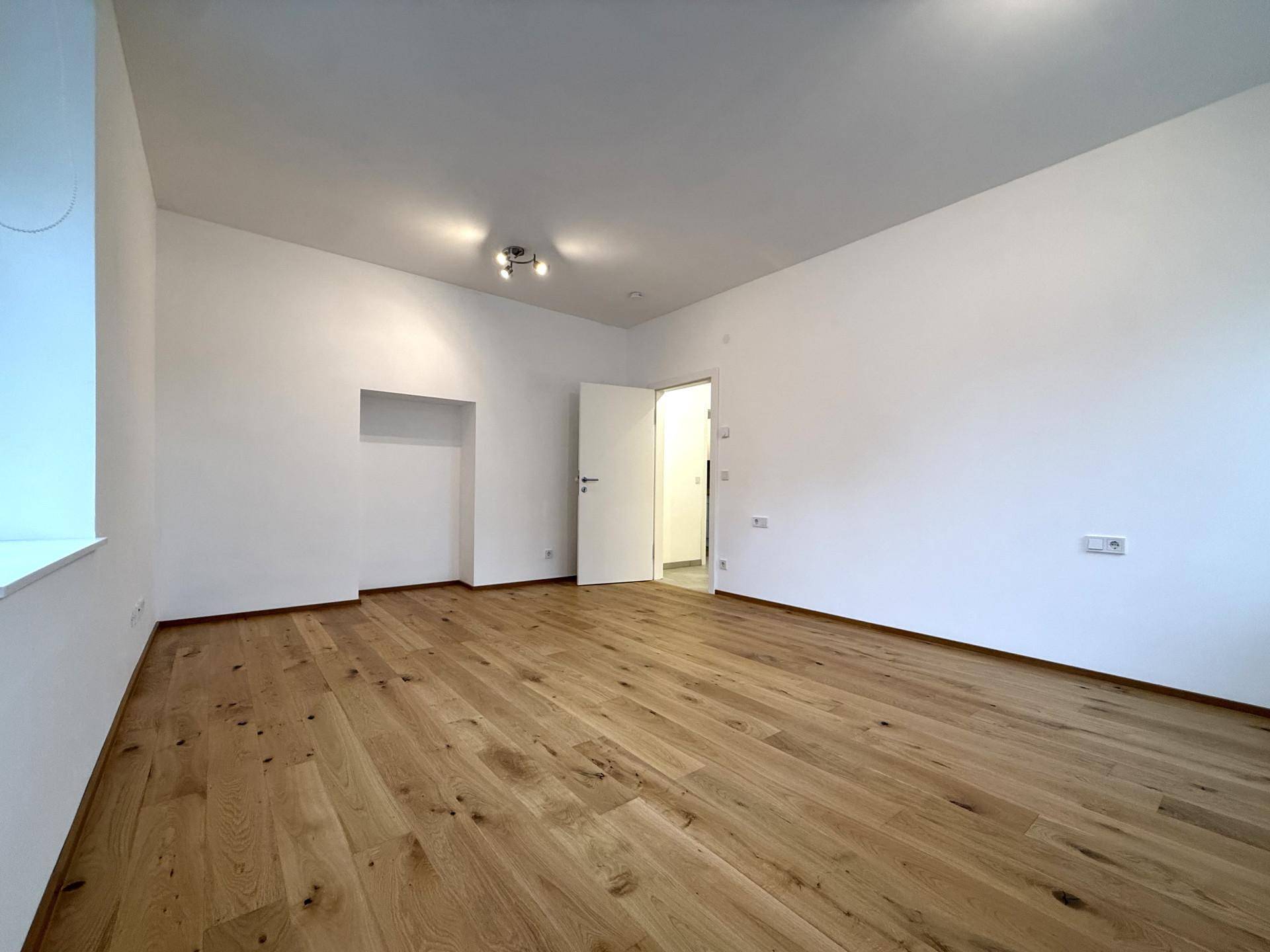 Geräumiger, heller Raum mit Holzboden und weiß gestrichenen Wänden, ideal als Wohnzimmer.