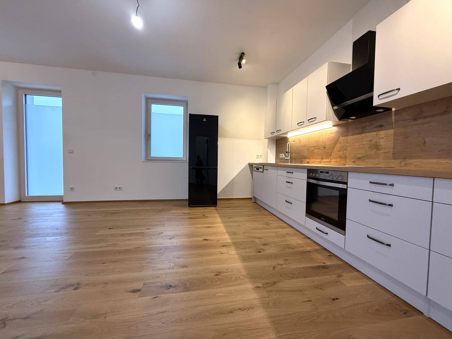 Offener Wohnbereich mit moderner Einbauküche, Holzboden und viel Tageslicht.