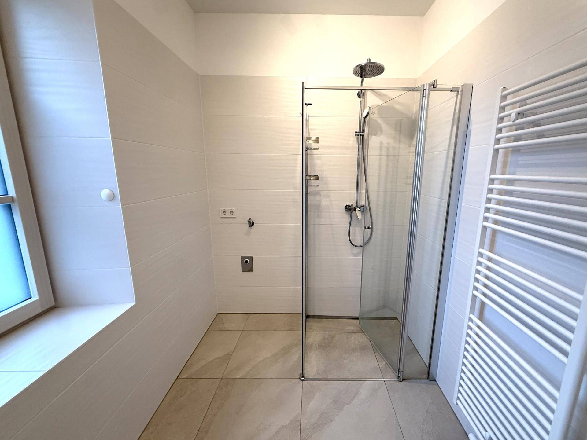 Helle Duschkabine mit Regendusche und Handtuchheizkörper in einem modern gefliesten Bad.