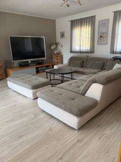 Gemütliches Wohnzimmer mit großem Ecksofa, Fernseher und hellem Laminatboden.