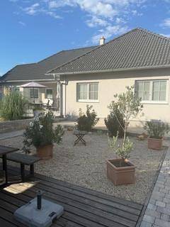 Hinterhof mit Kiesgarten, Holzterrasse und Topfpflanzen unter strahlend blauem Himmel.