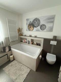 Elegantes Badezimmer mit Badewanne, Wand-WC und beheiztem Handtuchhalter.