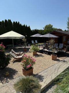 Weitläufiger Gartenbereich mit mehreren Sitzgelegenheiten, Sonnenschirmen und Pflanzen.