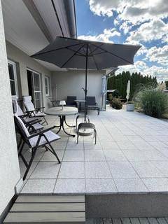 Große geflieste Terrasse mit Sonnenschirm und Gartenmöbeln für entspannte Stunden.