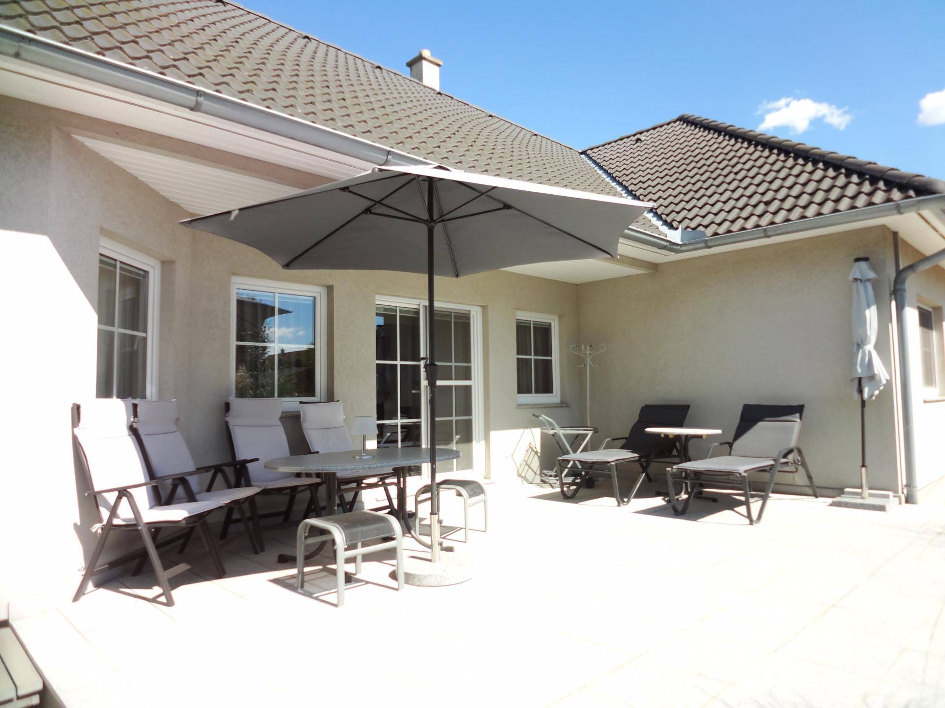 Große, sonnige Terrasse mit Gartenmöbeln und Sonnenschirm, ideal für Entspannung im Freien.