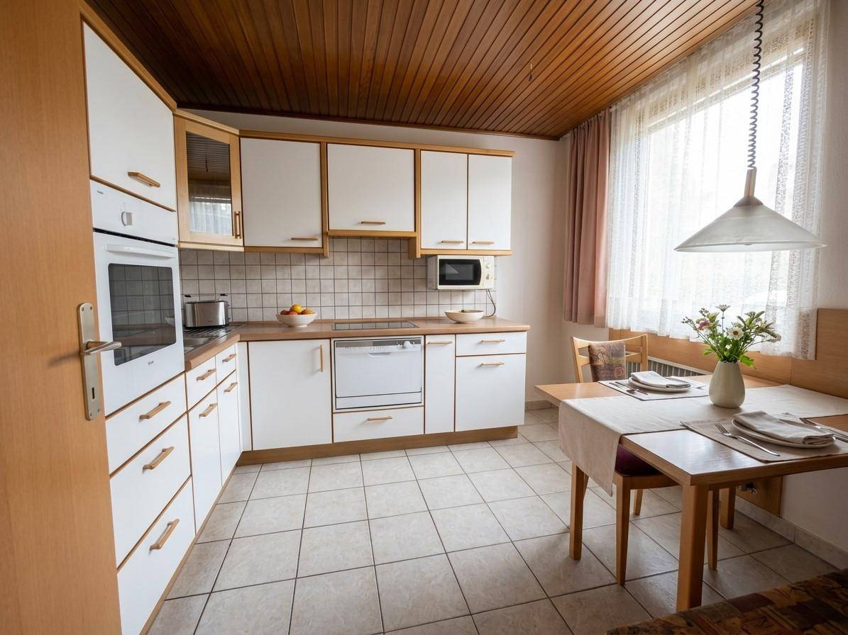 Gemütliche Küche mit weißen Einbauschränken, Fliesenboden und einem Essbereich am Fenster.