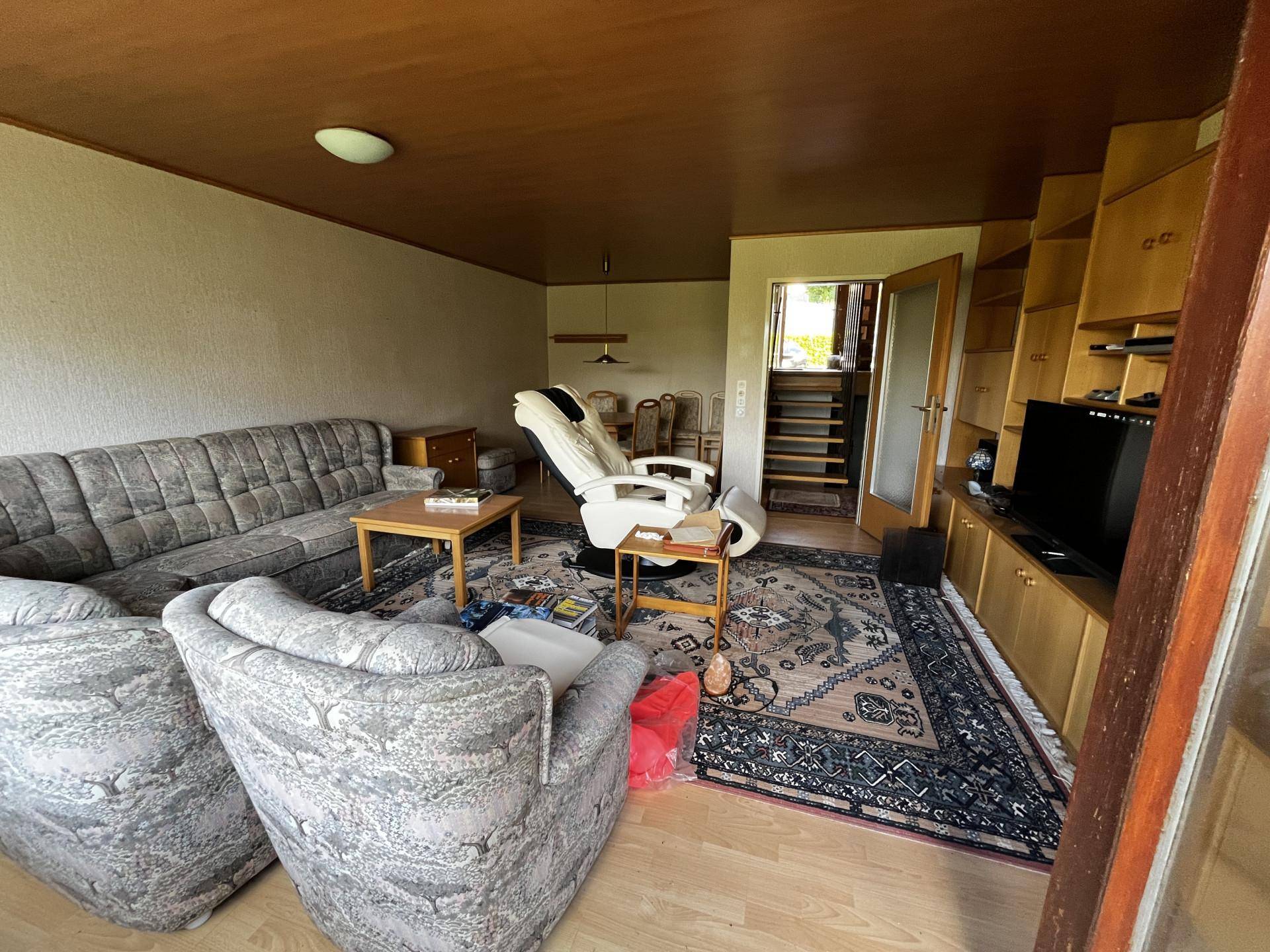 Geräumiger Wohnbereich mit Teppichboden, bequemen Sofas und einem Essbereich im Hintergrund.
