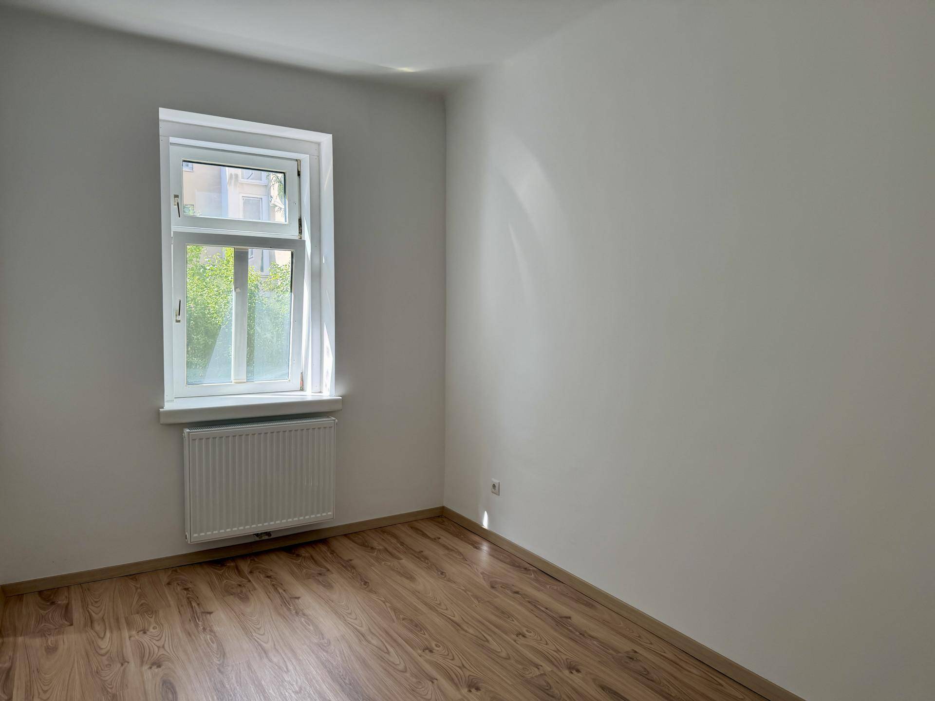 Leeres Zimmer mit Laminatboden und einem Fenster, ideal als Schlaf- oder Arbeitszimmer.