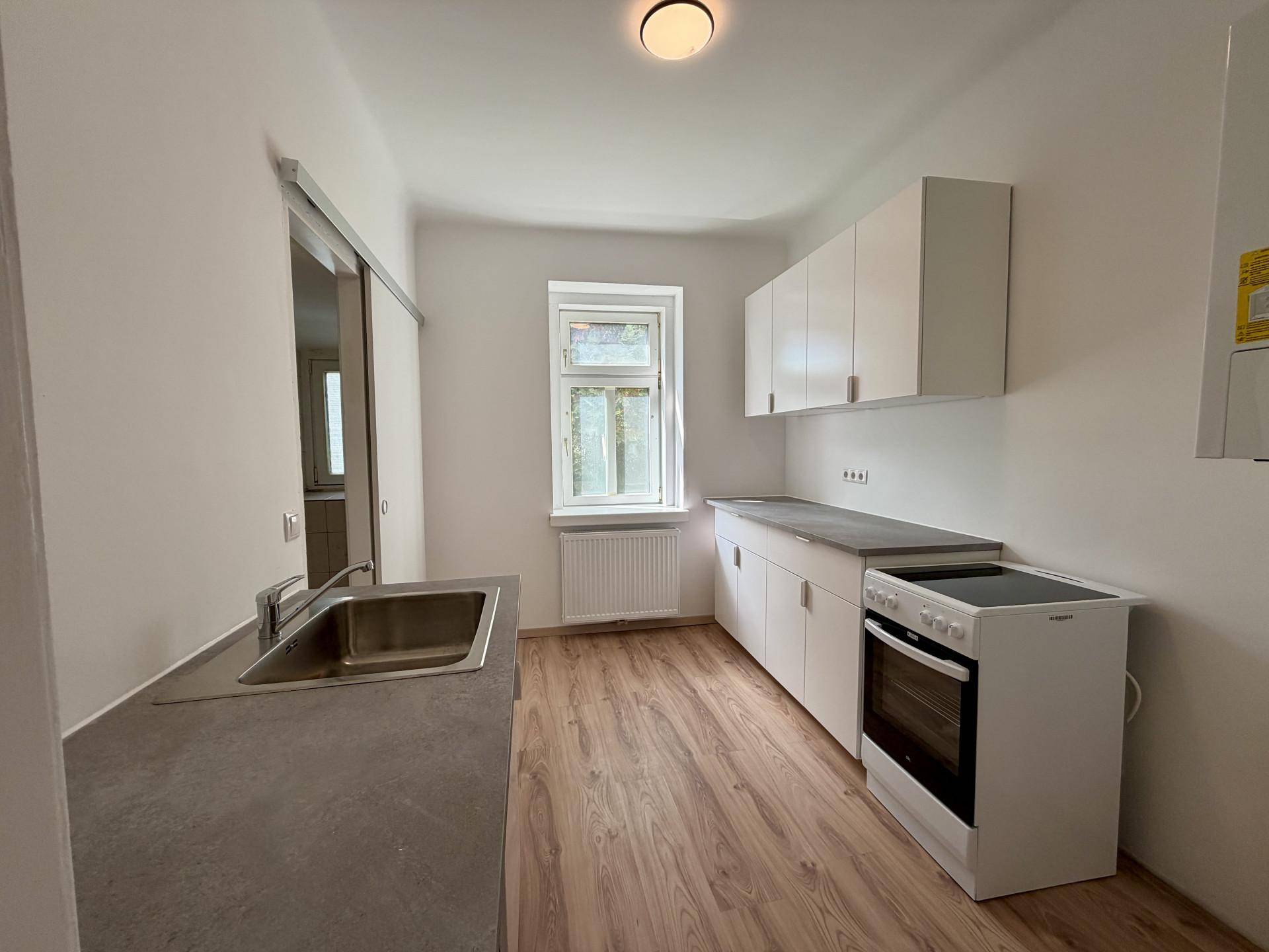 Helle Küche mit weißen Oberschränken, Spüle und einem Fenster für natürliches Licht.