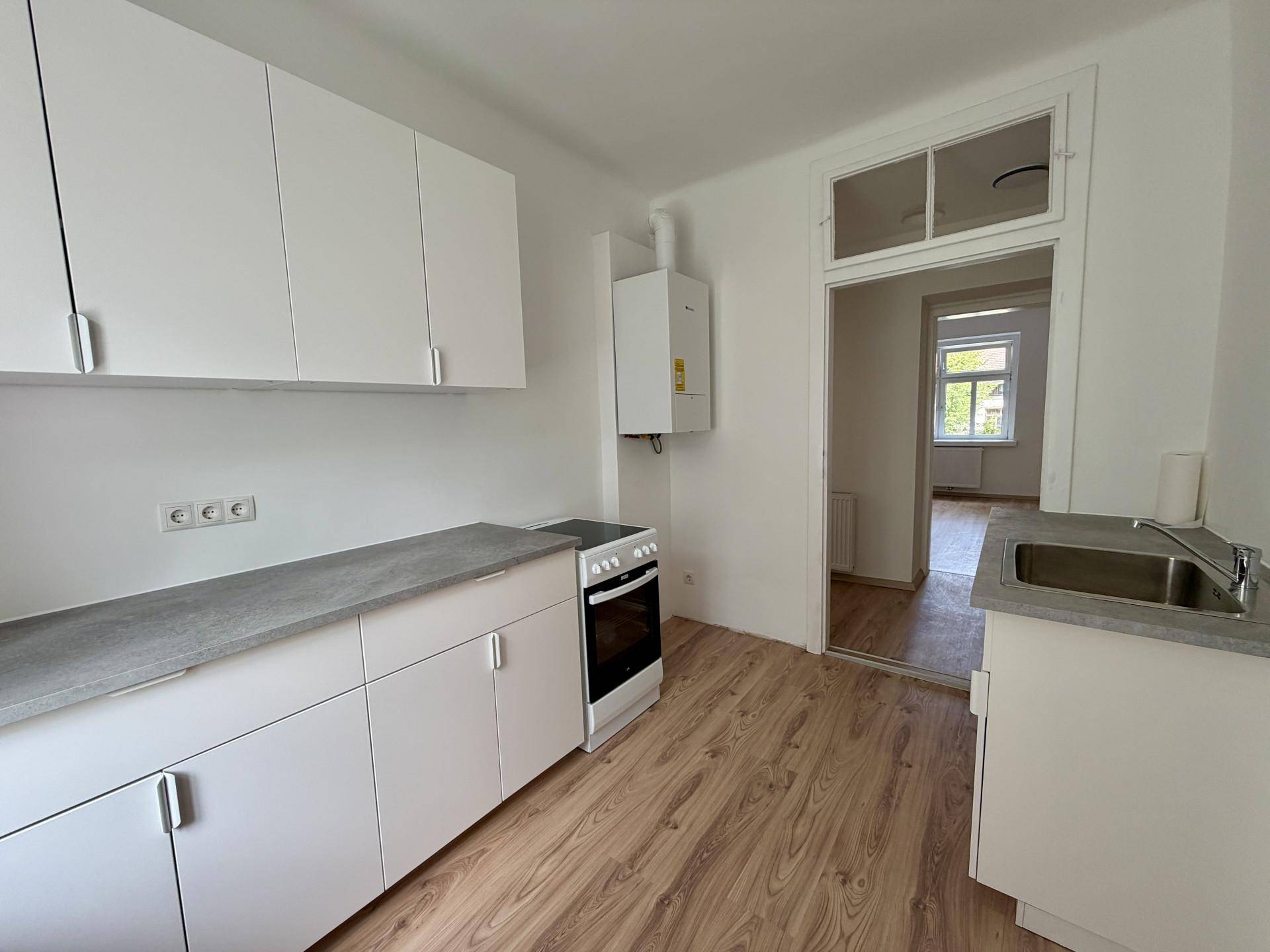Funktionale Küche mit weißen Schränken, grauer Arbeitsplatte und Blick in den angrenzenden Raum.