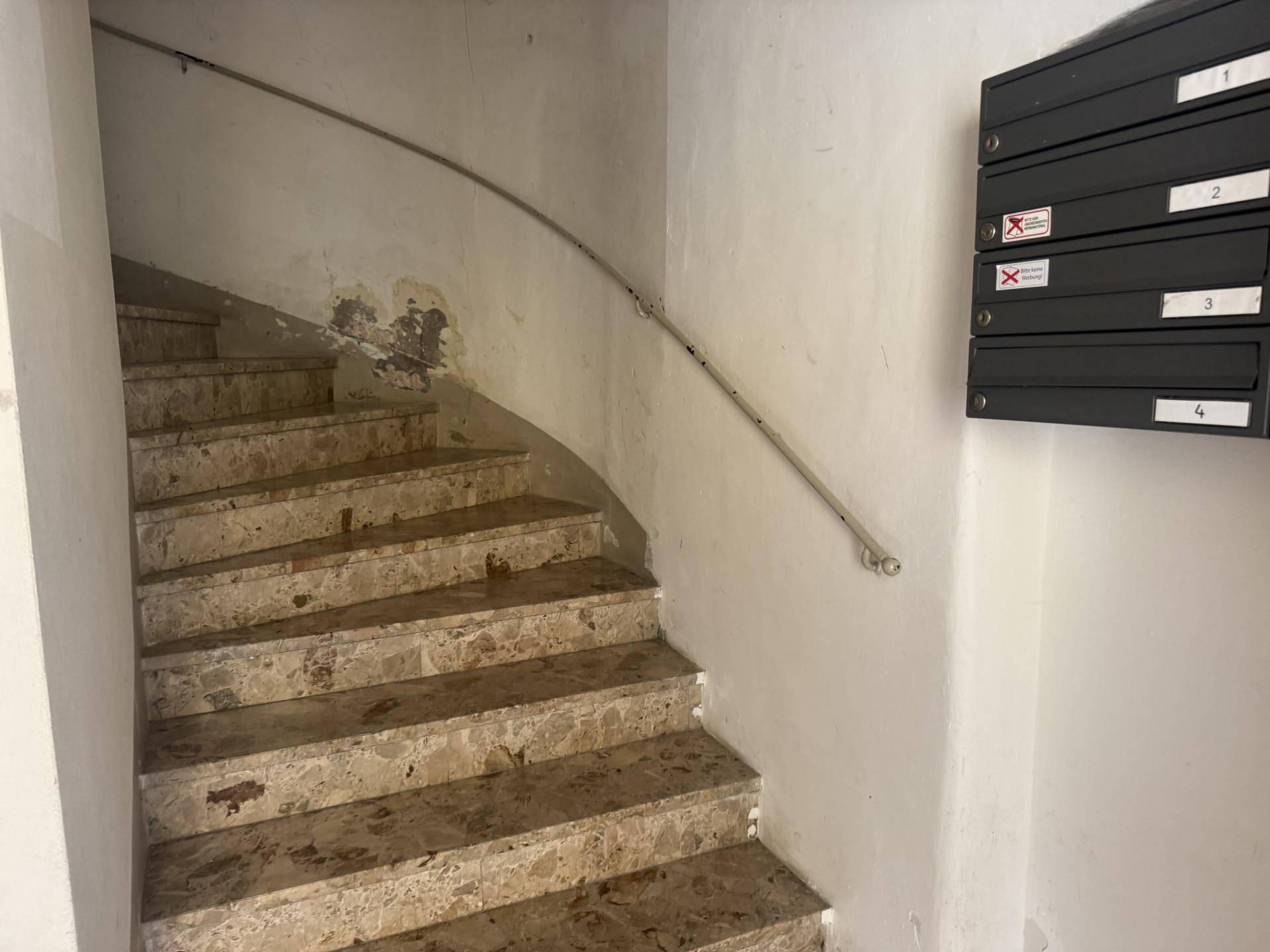 Treppenhaus mit Steinstufen und einem Handlauf, der zu den oberen Etagen führt.