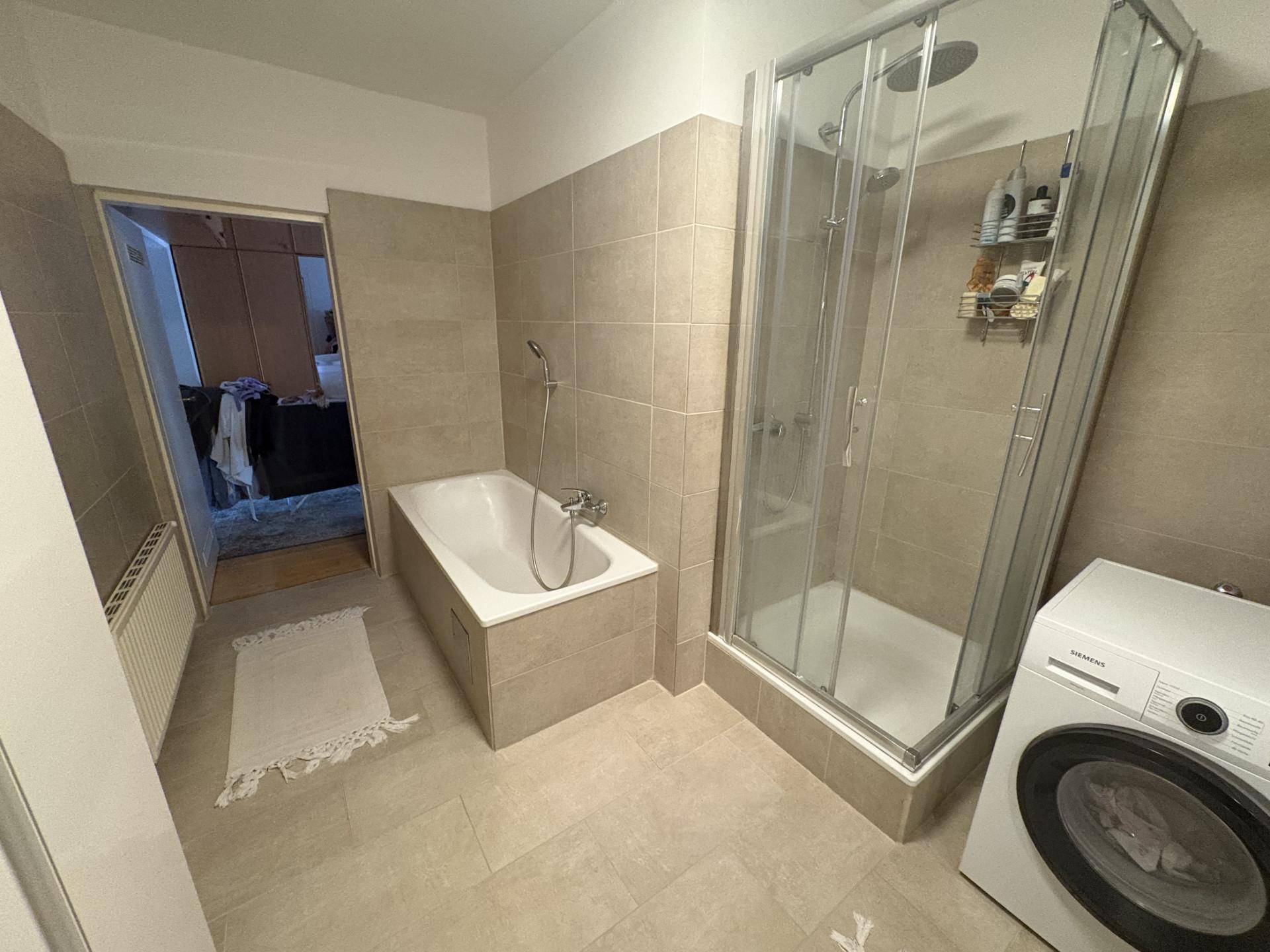 Modernes Badezimmer mit Badewanne, Duschkabine und Waschmaschine in hellen Fliesen.