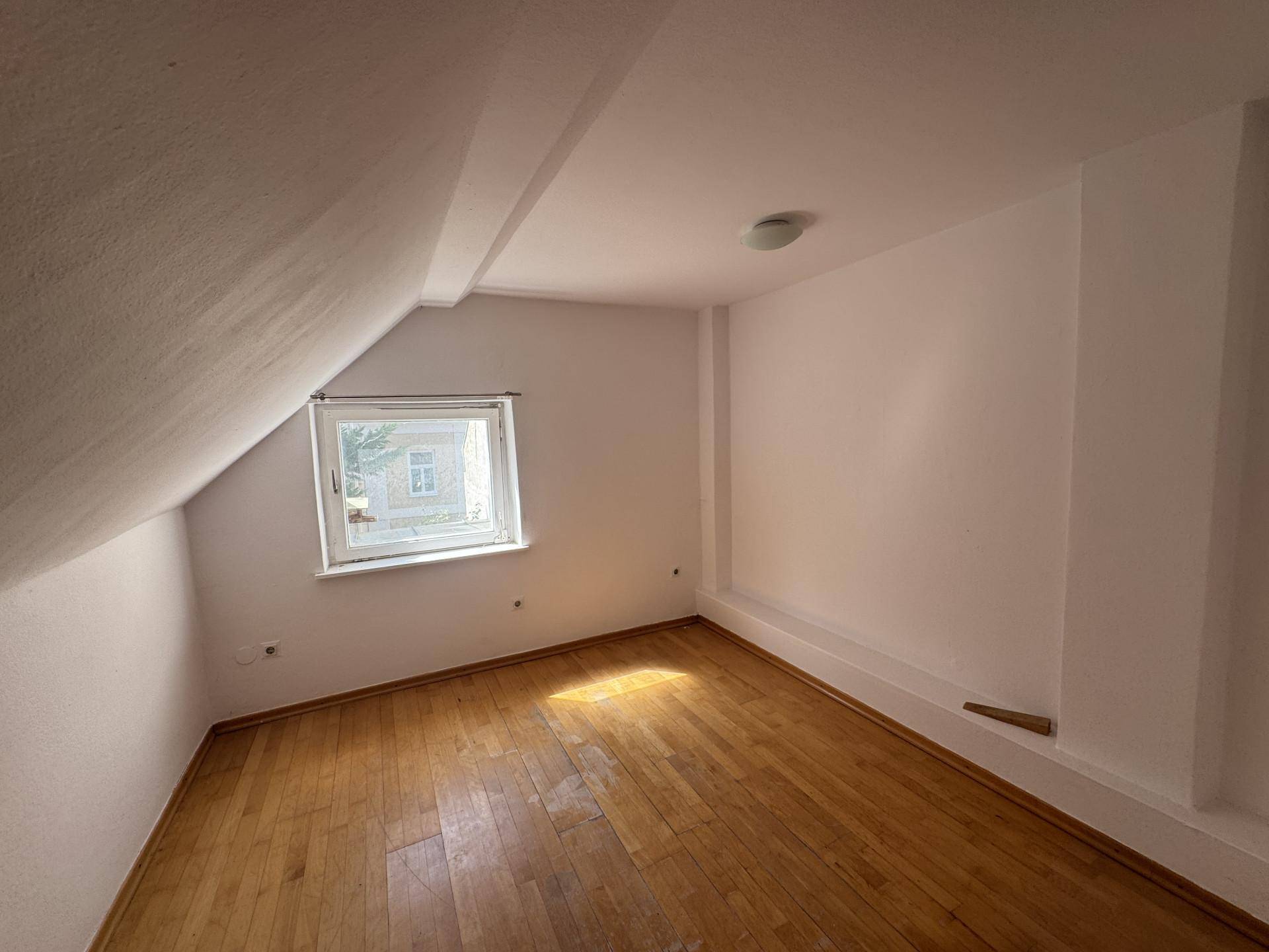 Helles Schlafzimmer im Dachgeschoss mit schrägen Wänden und Holzfußboden.