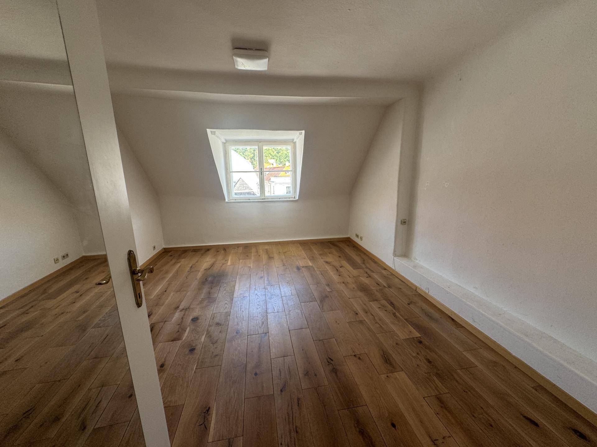Geräumiges Schlafzimmer im Dachgeschoss mit Holzdielenboden und Dachfenster.