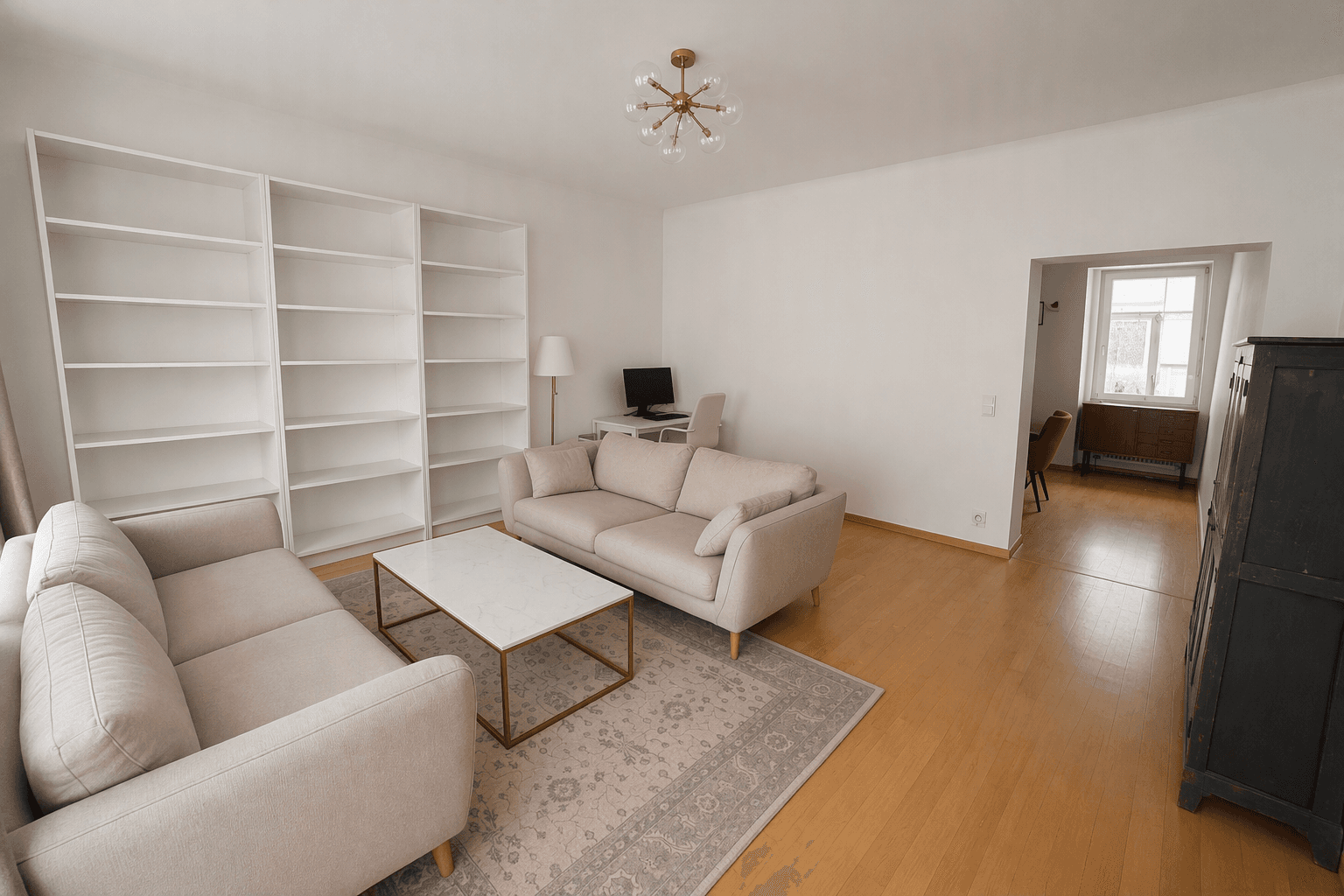 Geräumiges Wohnzimmer mit hellen Sofas, Bücherregal und Holzboden, offen zu einem weiteren Raum.