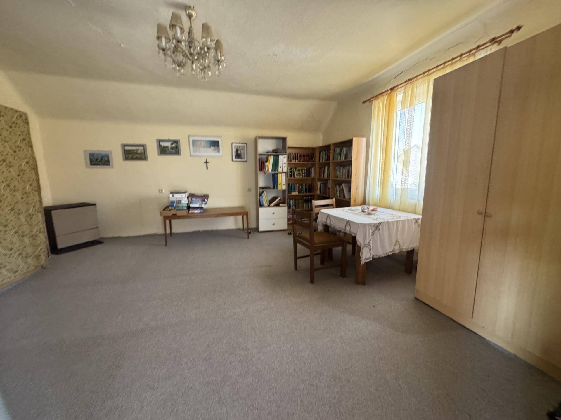 Großer Wohnraum mit Teppichboden, Bücherregal und einem Esstisch unter einem Kronleuchter.