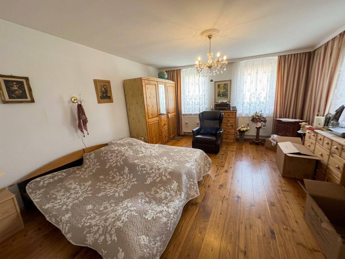 Geräumiges Schlafzimmer mit Holzboden, Doppelbett und traditionellen Holzmöbeln unter einem Kronleuchter.
