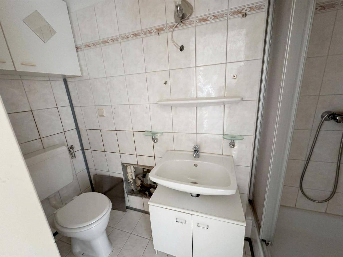 Kleines Badezimmer mit WC, Waschbecken und Duschbereich, ausgestattet mit einfachen Fliesen.