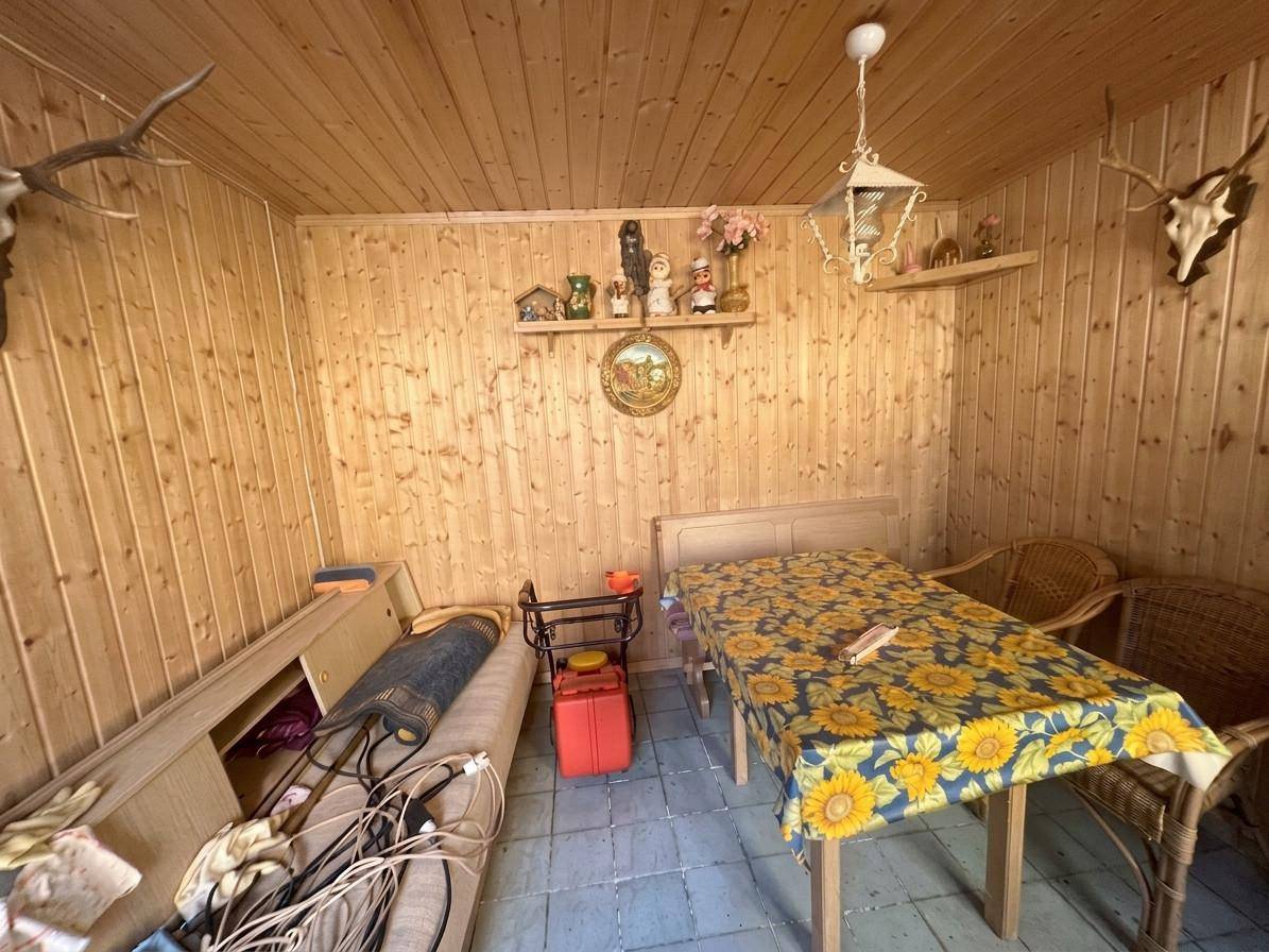 Rustikaler Raum mit Holzverkleidung, gefliestem Boden und einem Tisch mit Sonnenblumenmuster.