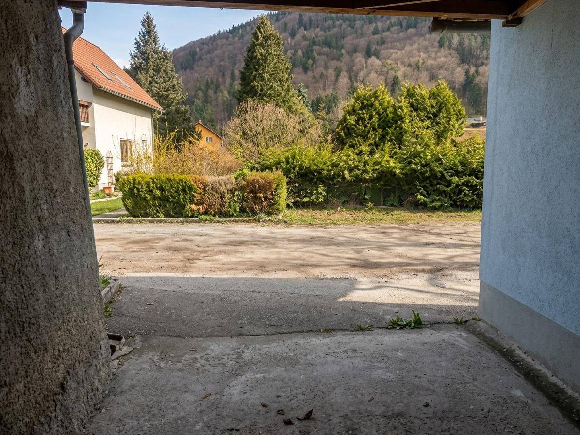 Blick aus einer Öffnung auf einen Schotterplatz mit Hecken und bewaldeten Hügeln im Hintergrund.