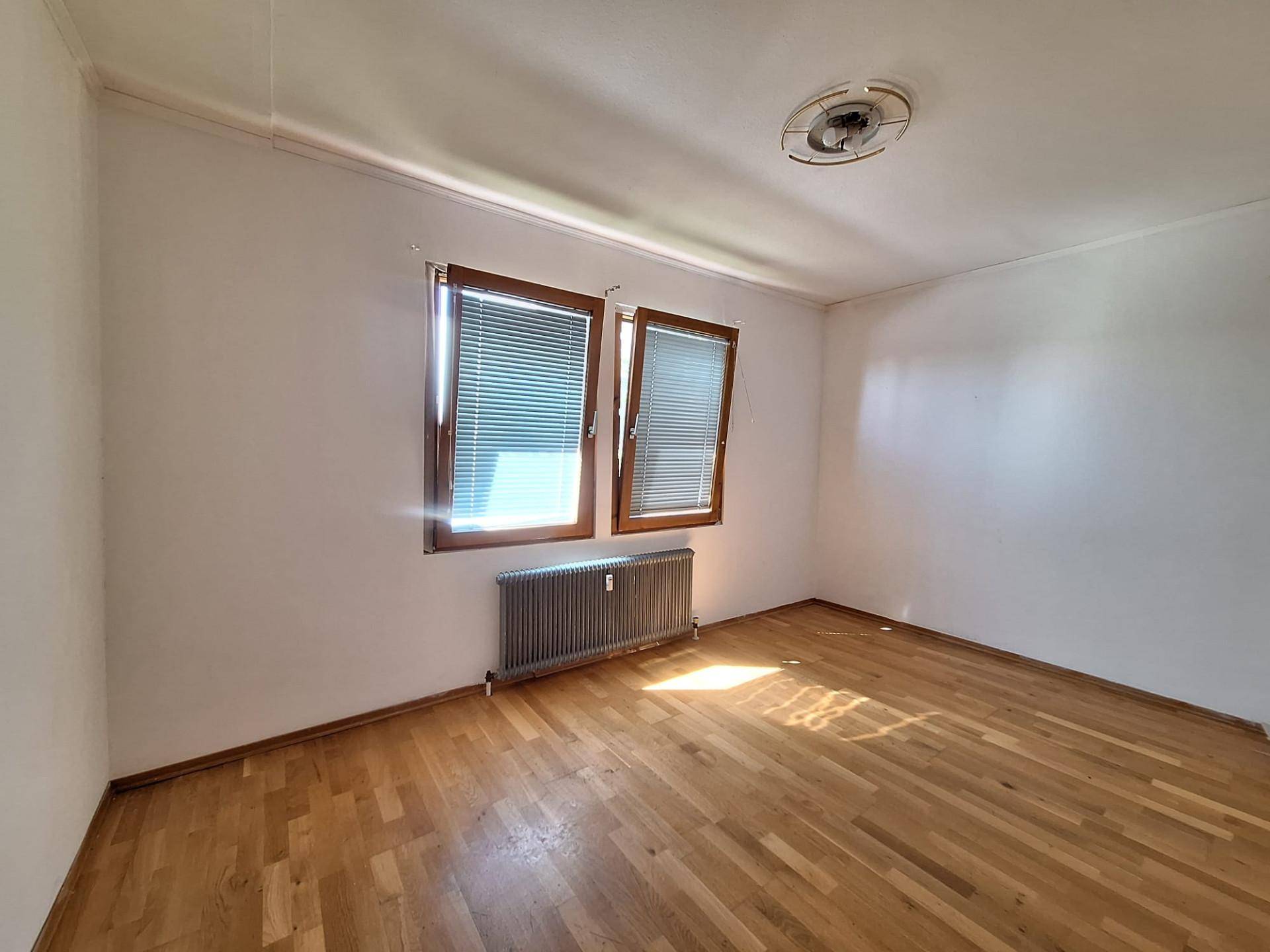 Helles Schlafzimmer mit Parkettboden und zwei Fenstern, bietet viel Tageslicht.