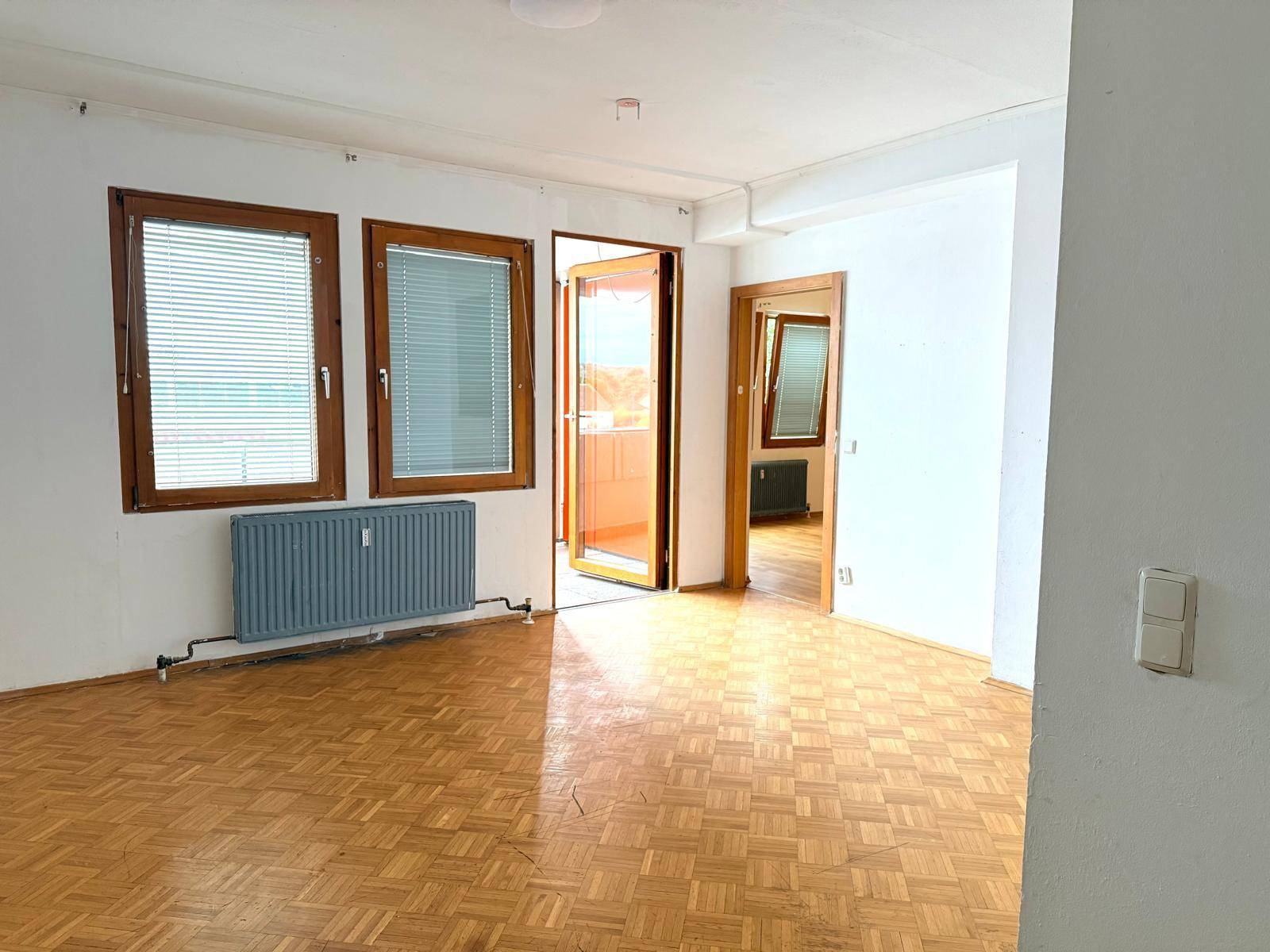 Geräumiges Wohnzimmer mit Parkettboden und Zugang zu einem Balkon, hell und einladend.