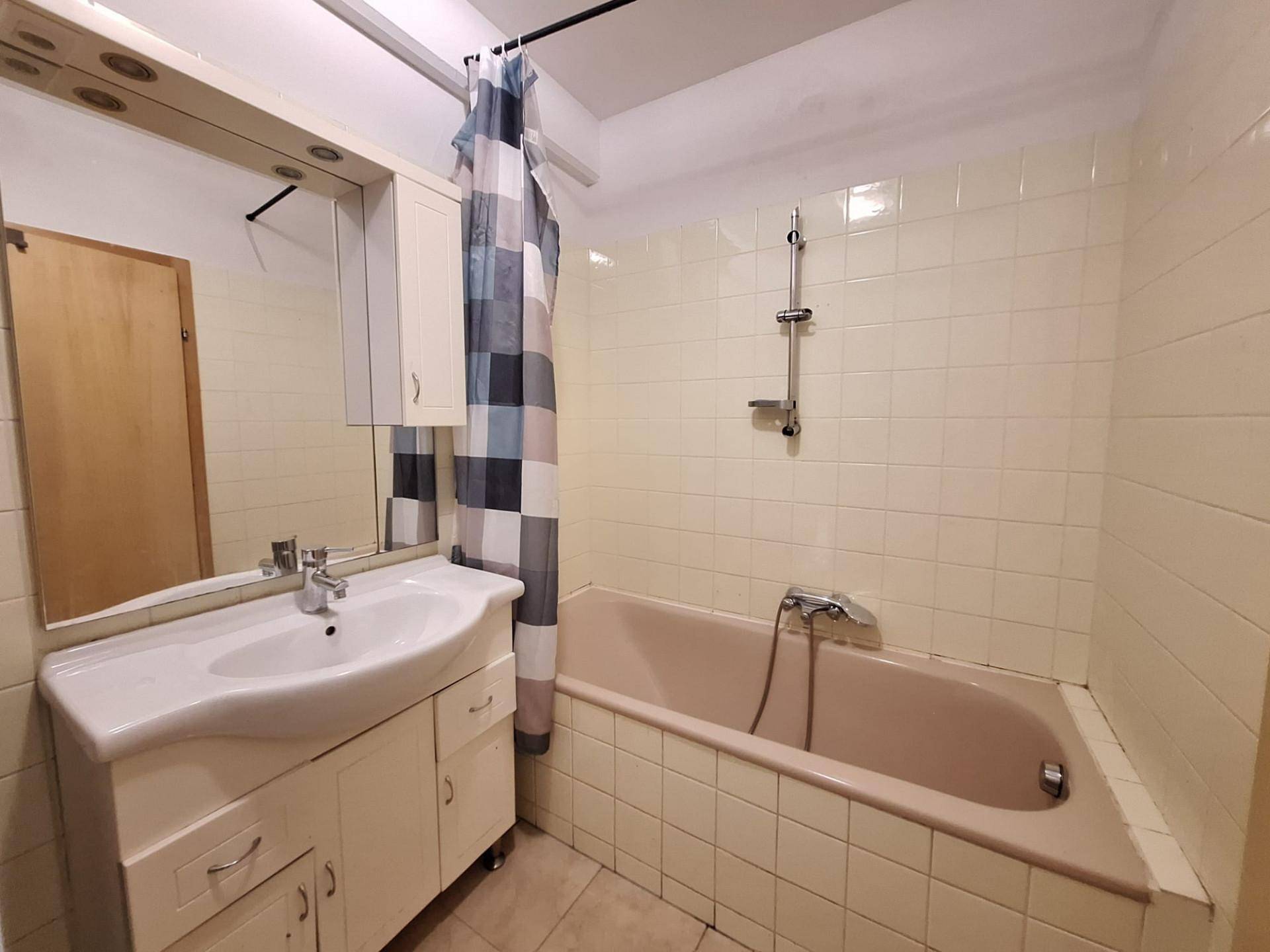 Badezimmer mit Badewanne, Waschbecken und hellen Fliesen, funktional und gepflegt im Stil der 80er.