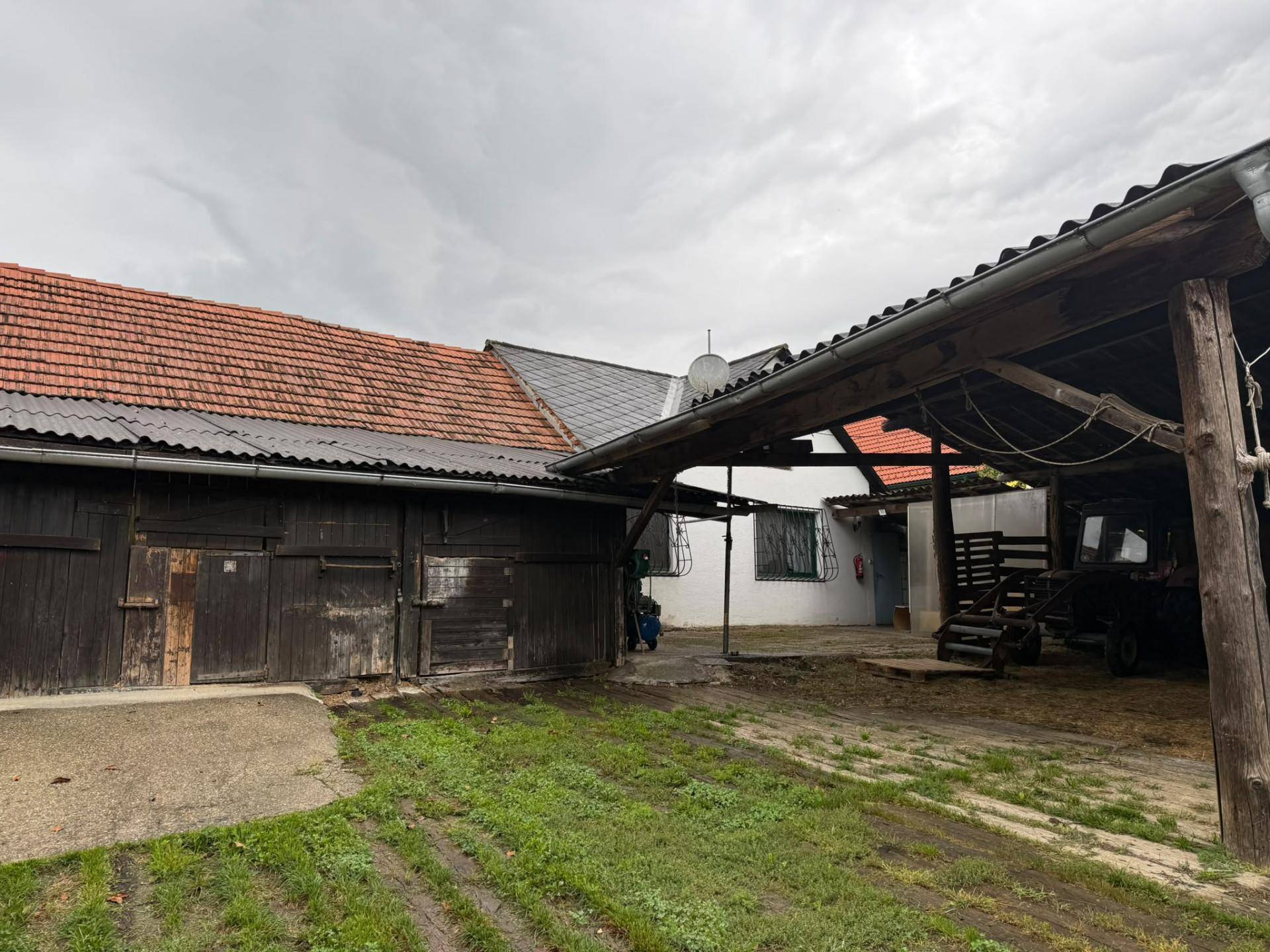 Außenbereich mit Scheune, Carport und weiteren Nebengebäuden, umgeben von Grünflächen und Wegen.