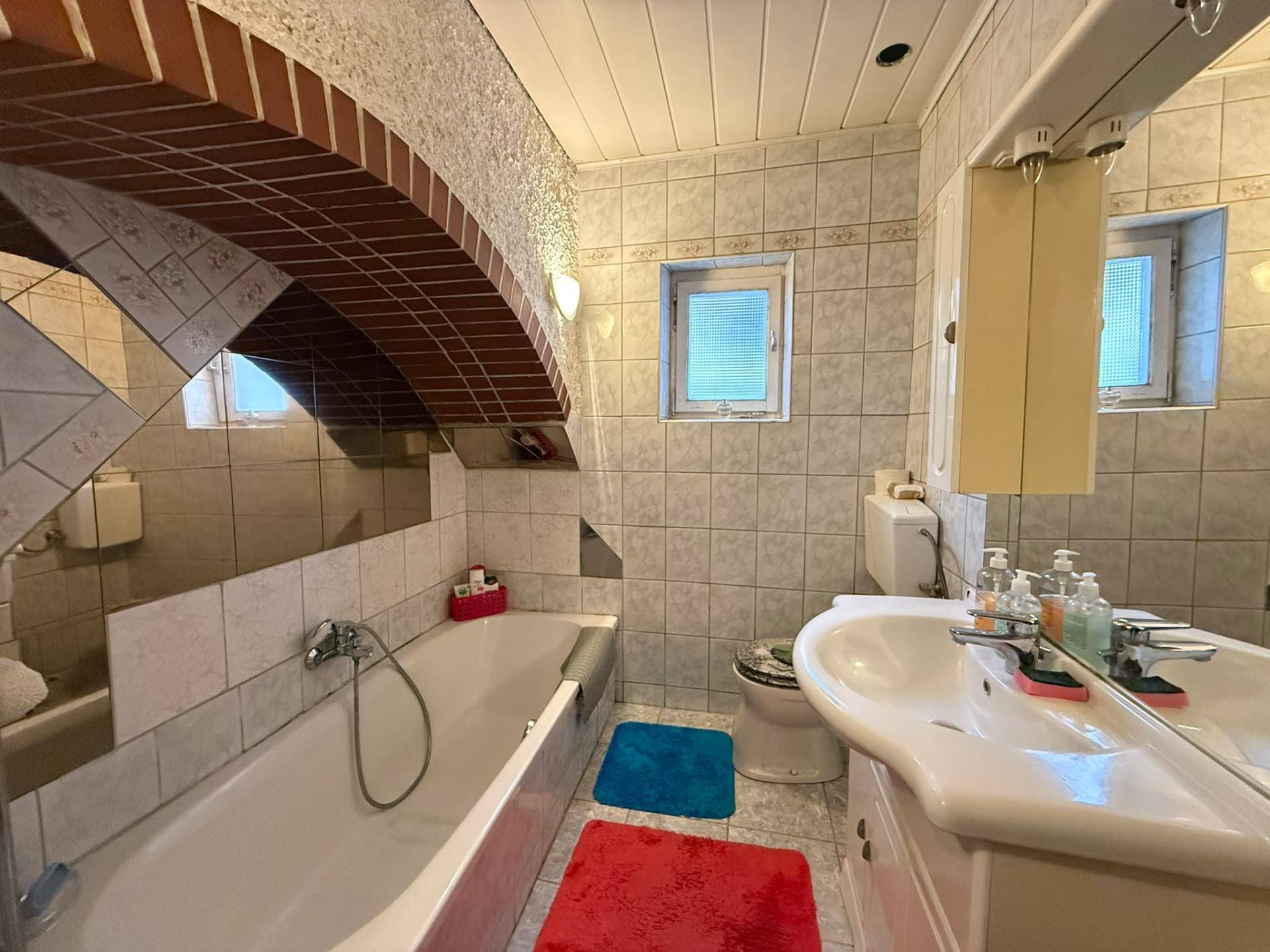 Badezimmer mit Badewanne, Waschbecken und WC, unter Dachschräge mit Holzbalken und Fliesen.